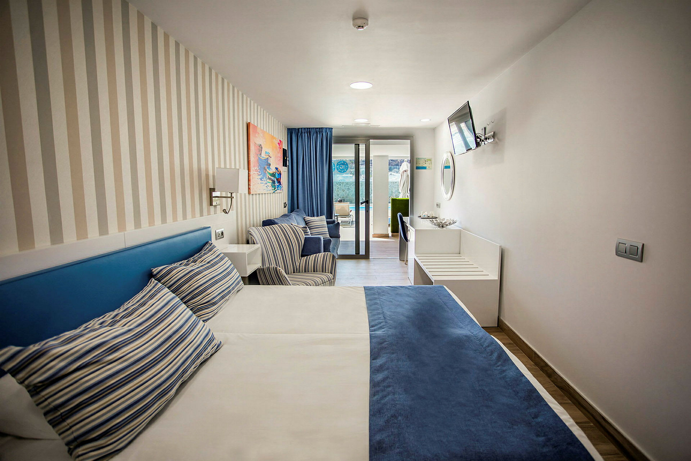 Hotellrum med en säng, två stolar och fönster mot en uteplats. (AI-genererad text)