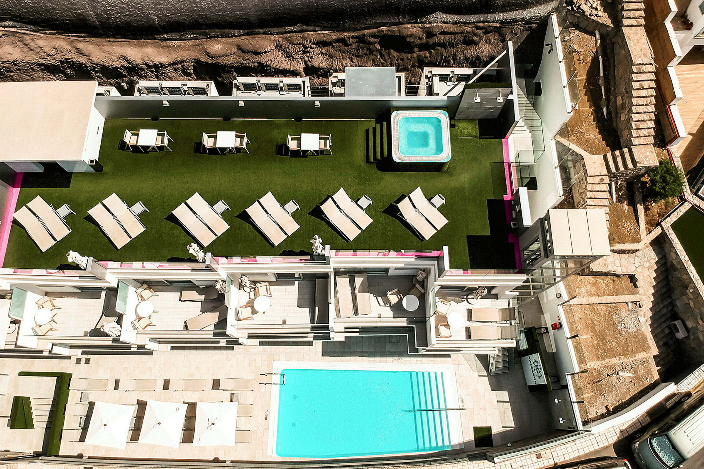 Vy från ovan av hotellområde med grönskande gräsmatta, solstolar, bubbelpool och pool. (AI-genererad text)