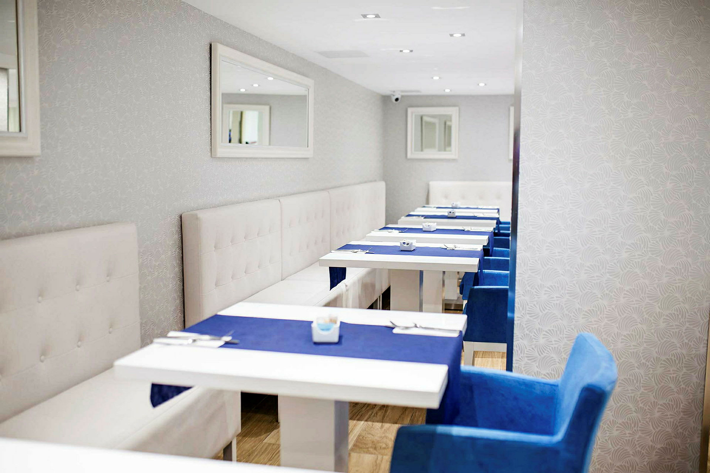 En restaurang med vita bord, blå stolar och vita väggar med en spegel. (AI-genererad text)