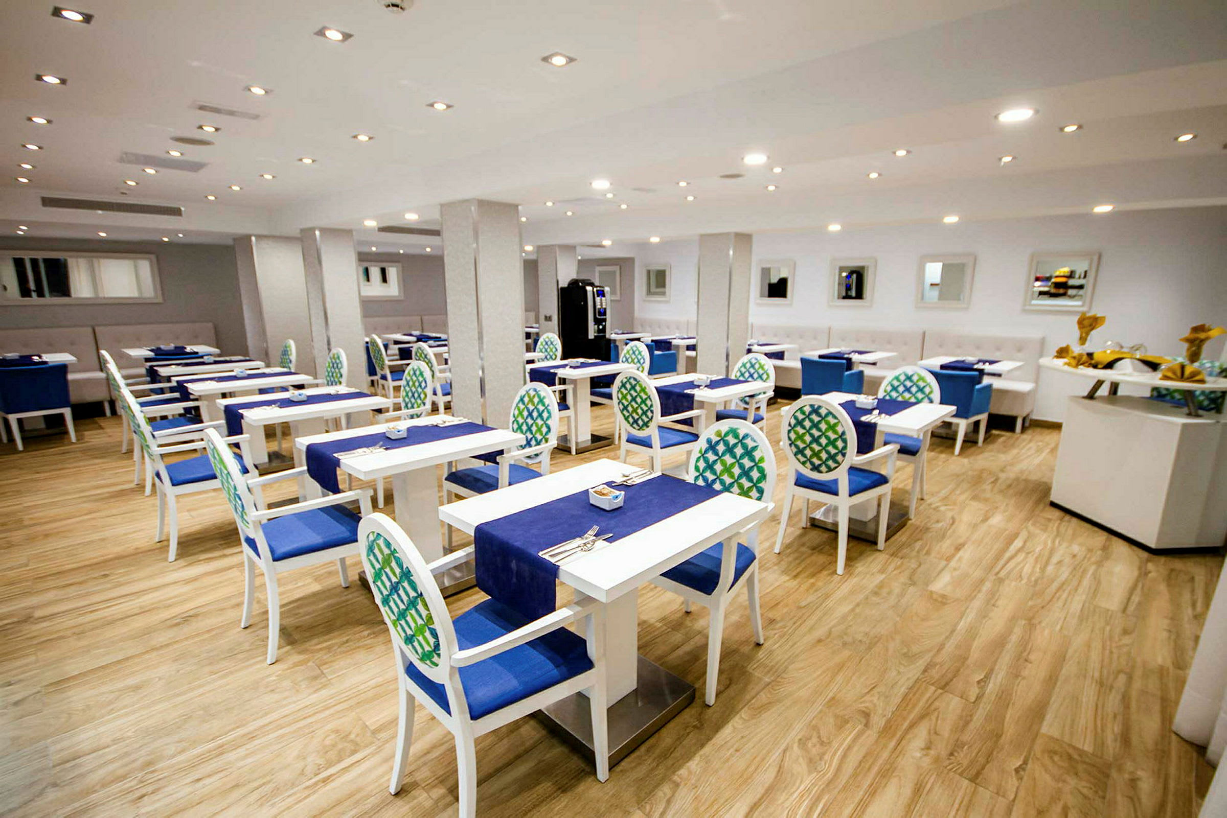 En restaurang med uppsättning av bord och stolar med blå och gröna detaljer. (AI-genererad text)