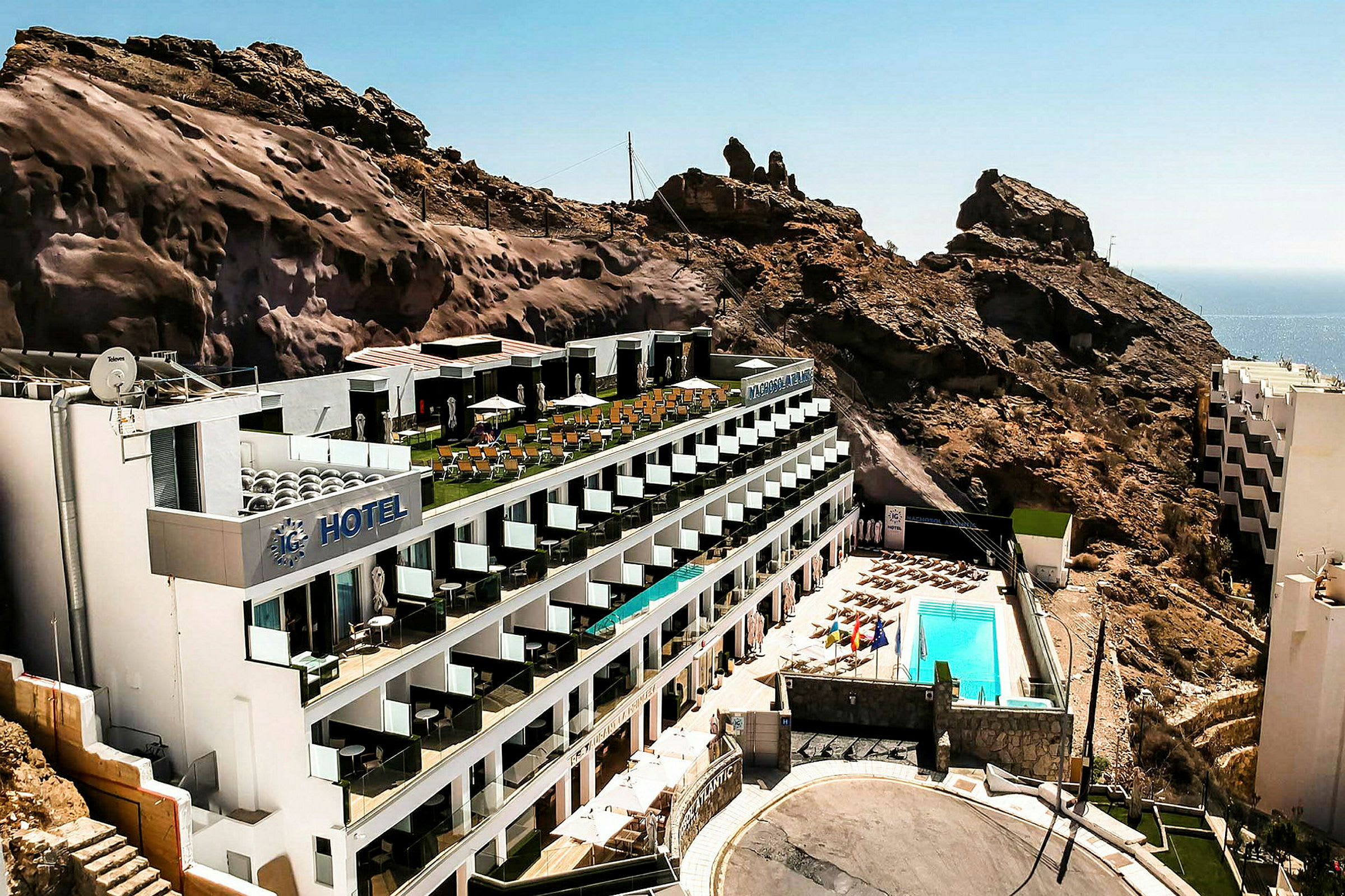 Ett hotell beläget vid en bergssluttning med en poolområde och havsutsikt. (AI-genererad text)