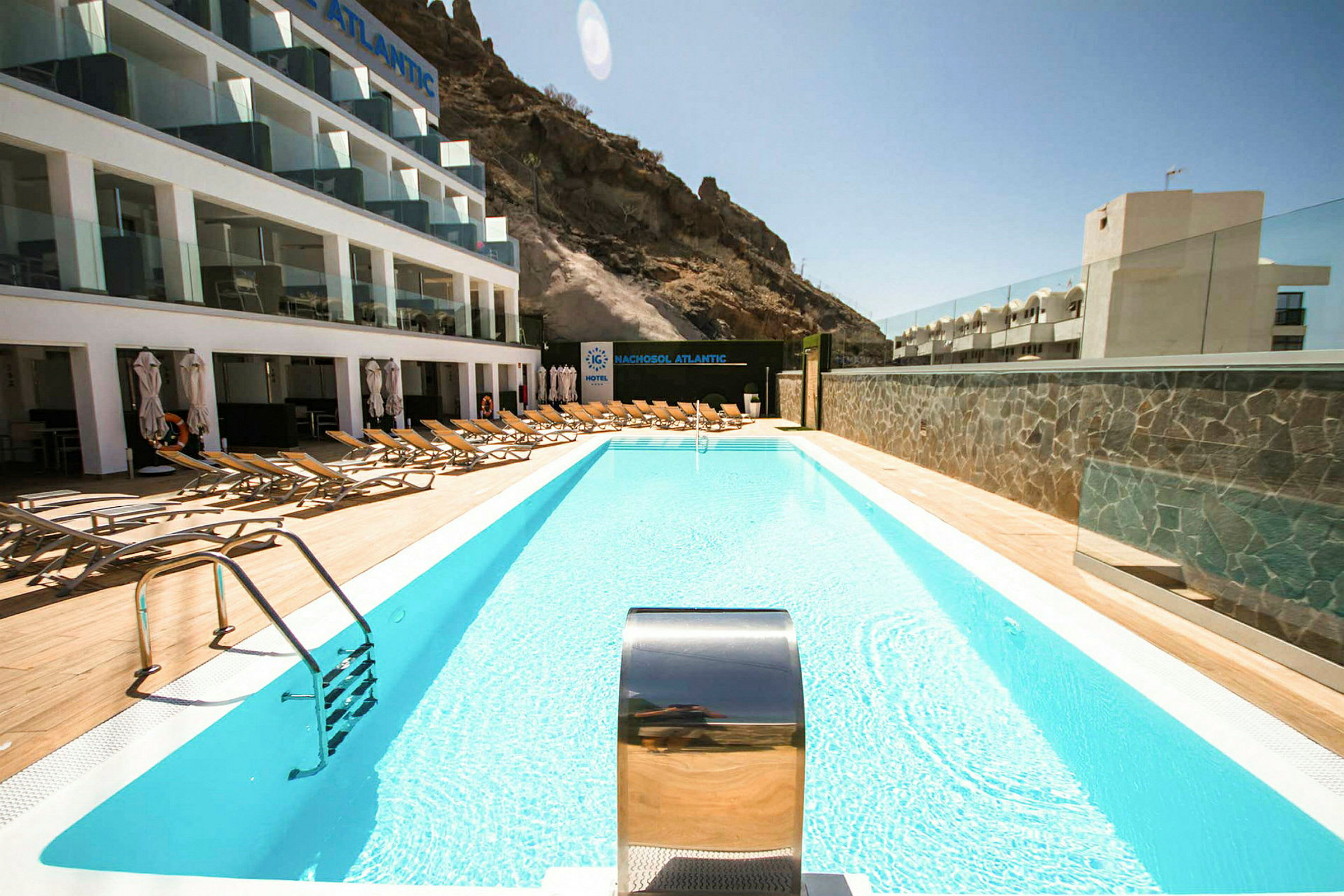 Utomhuspool med solstolar och hotellbyggnad i bakgrunden. (AI-genererad text)
