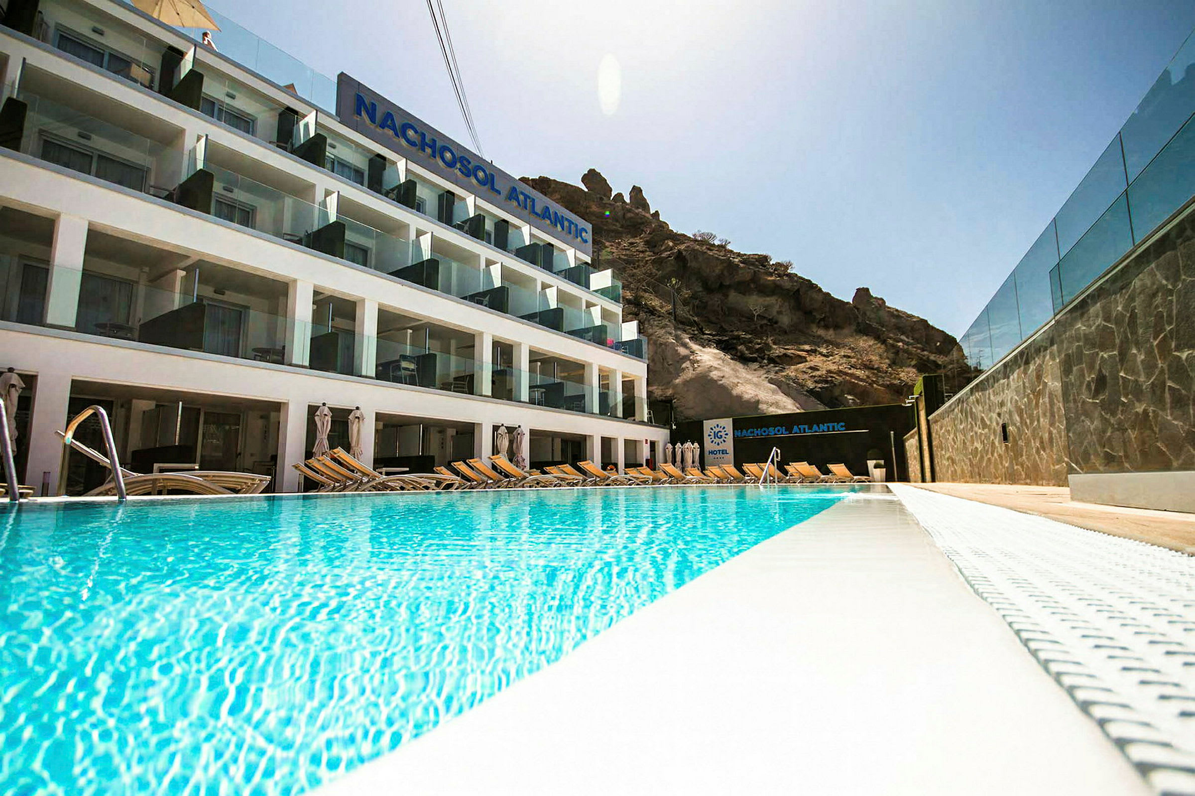 Hotell Nachosol Atlantic med pool framför och berg i bakgrunden. (AI-genererad text)