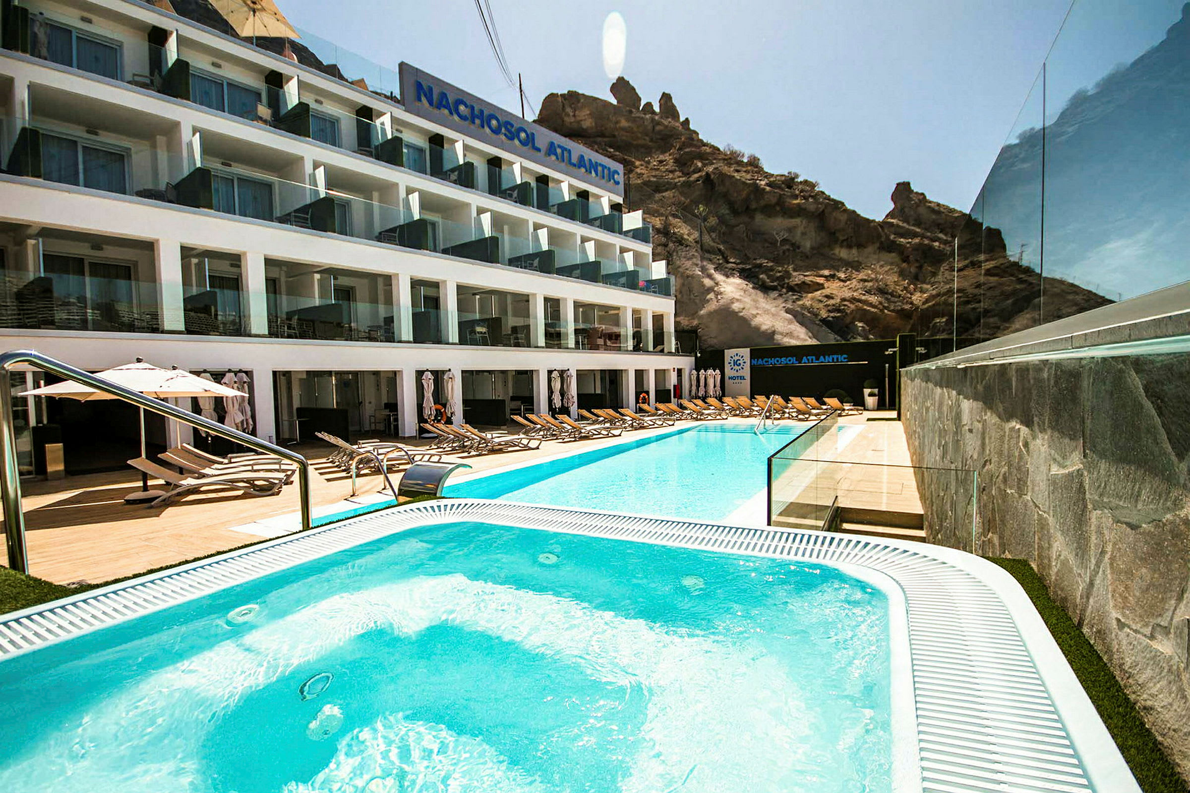 Hotellfasad med pool och solstolar i förgrunden. (AI-genererad text)