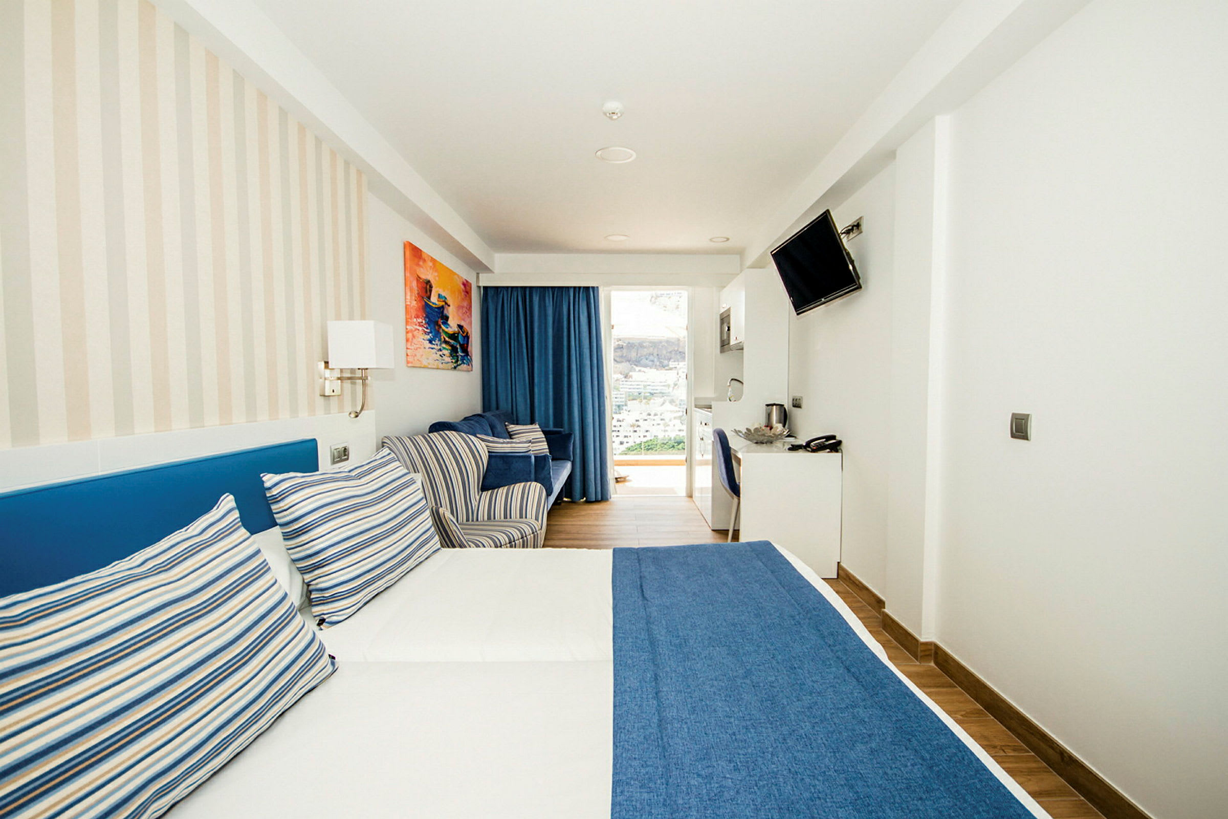 Ett hotellrum med en dubbelsäng med blå sängöverkast och randiga kuddar. (AI-genererad text)