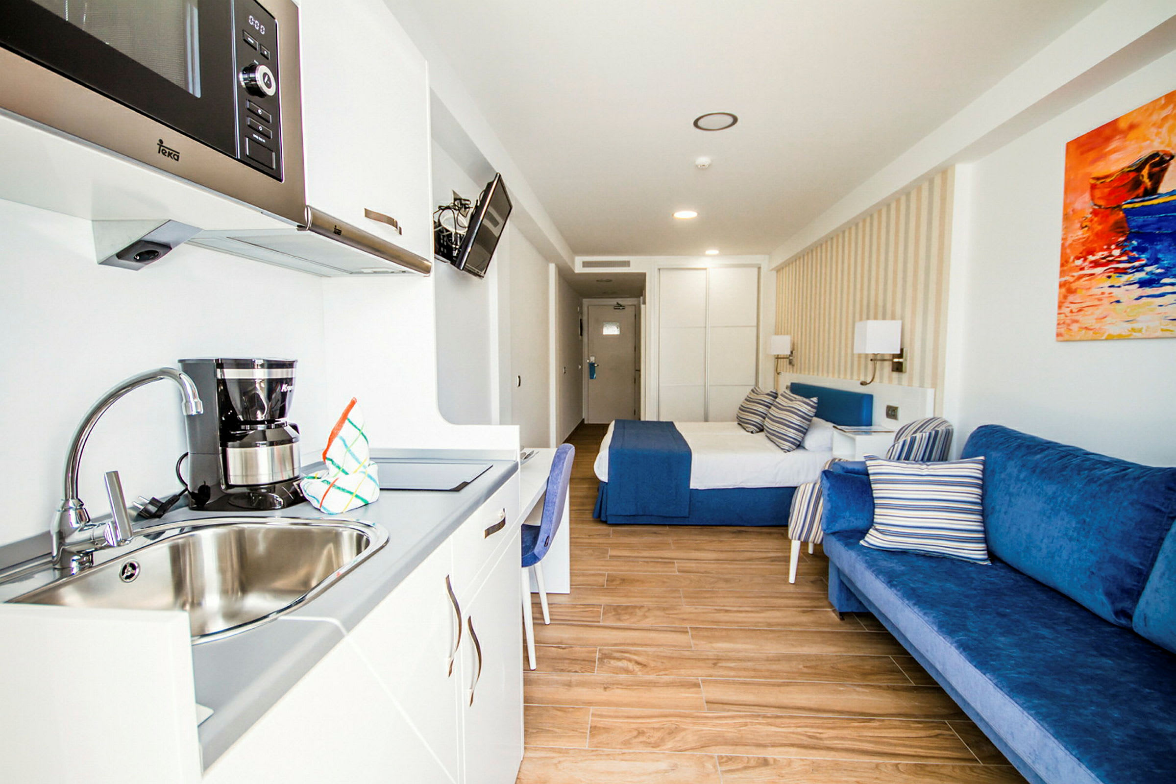 Ett hotellrum med en säng, blå soffa och köksdel med diskho. (AI-genererad text)
