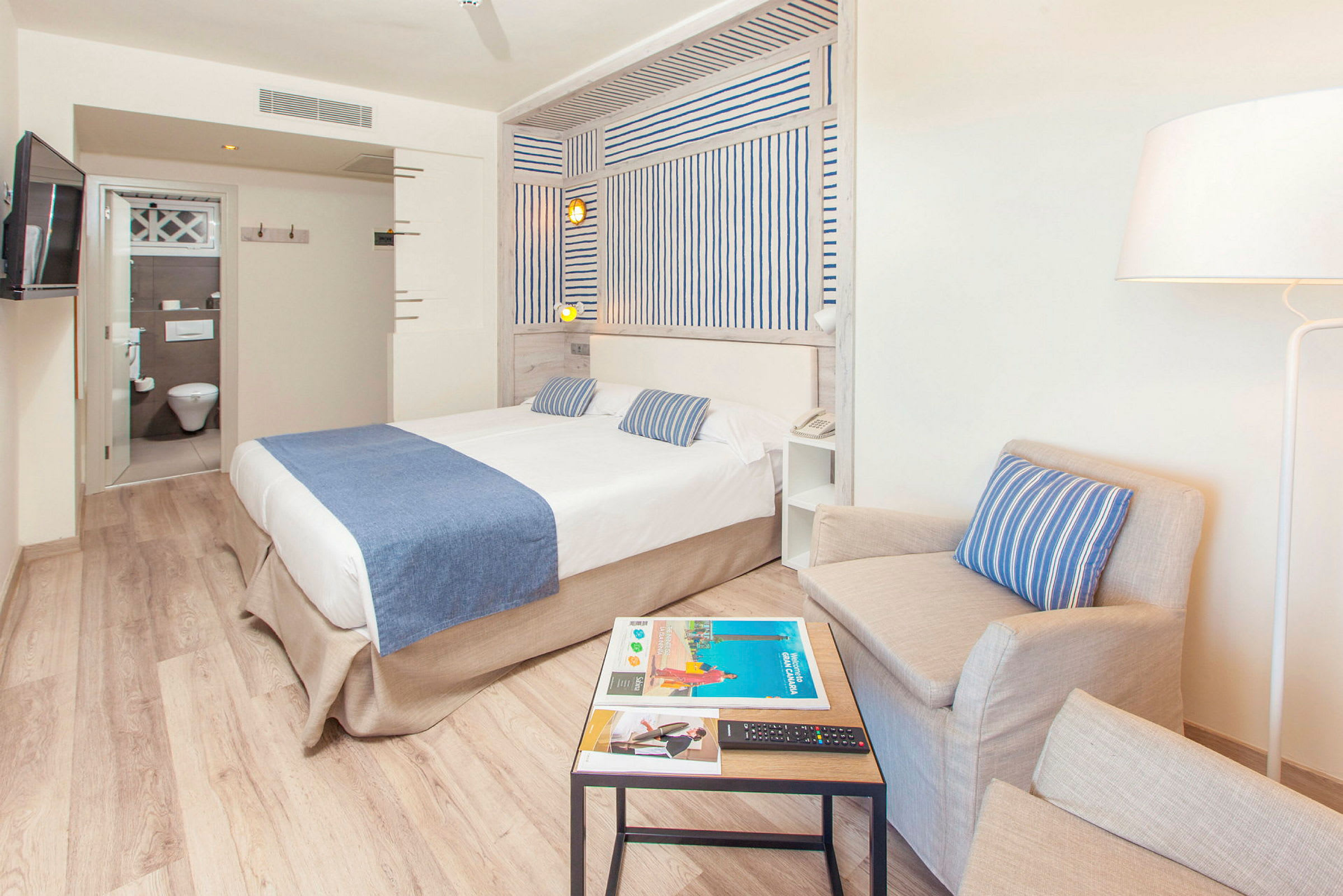 Hotellrum med säng, fåtölj och bord. (AI-genererad text)