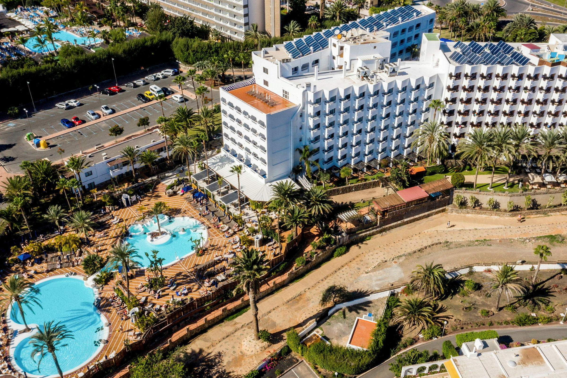 Flygfoto av hotellområde med flera pooler och omgivande grönska. (AI-genererad text)