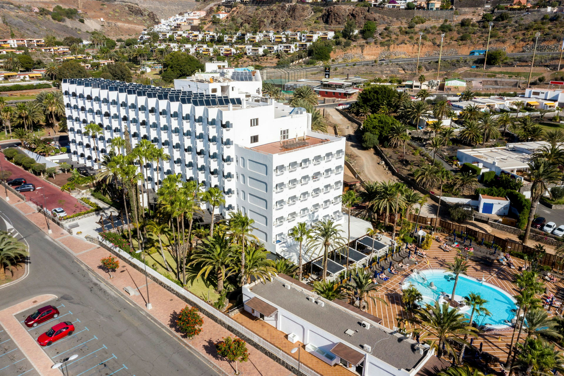Ett hotellkomplex med pool och palmträd omgiven av berg och grönska. (AI-genererad text)