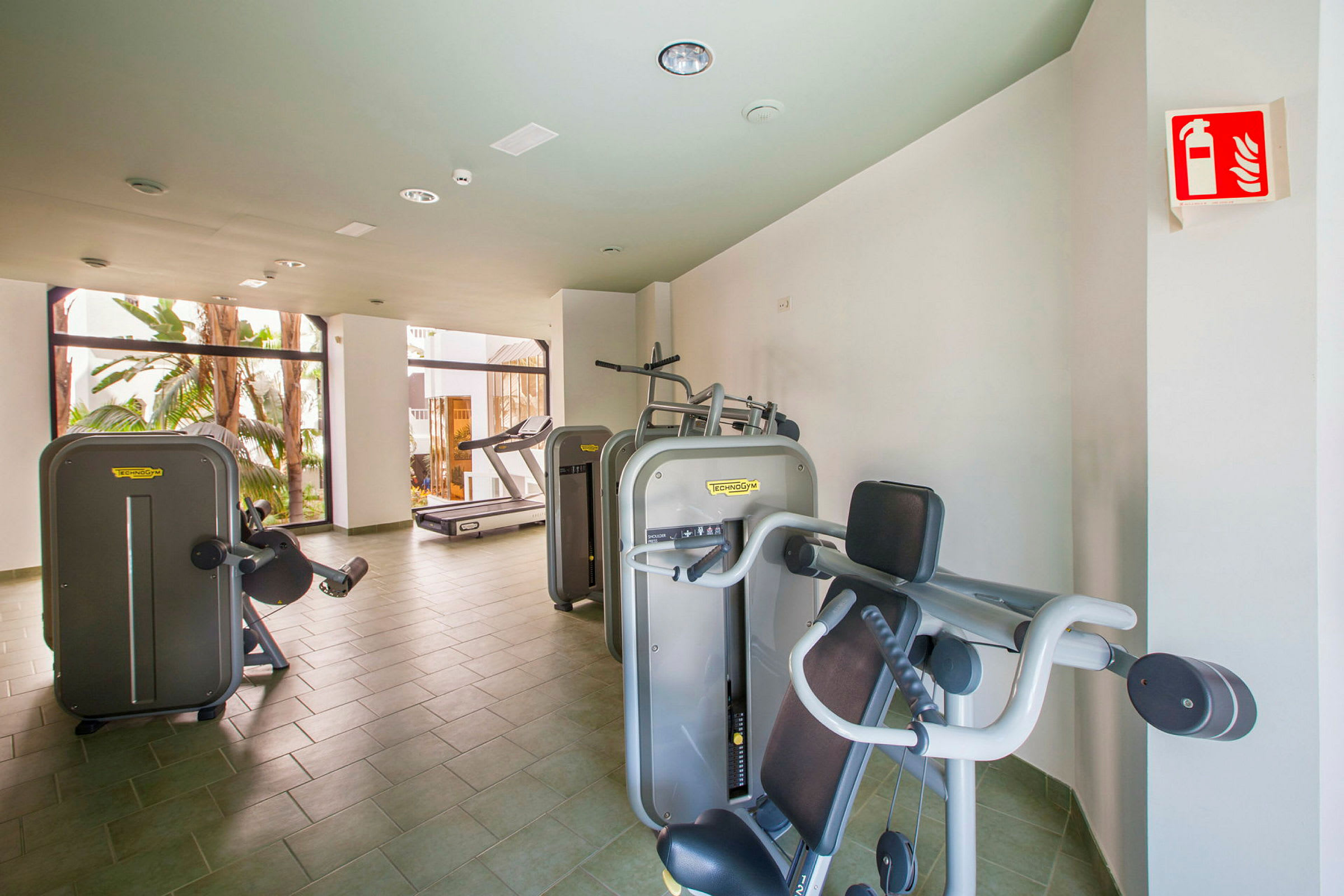 Gym med träningsmaskiner och utsikt mot fönster. (AI-genererad text)