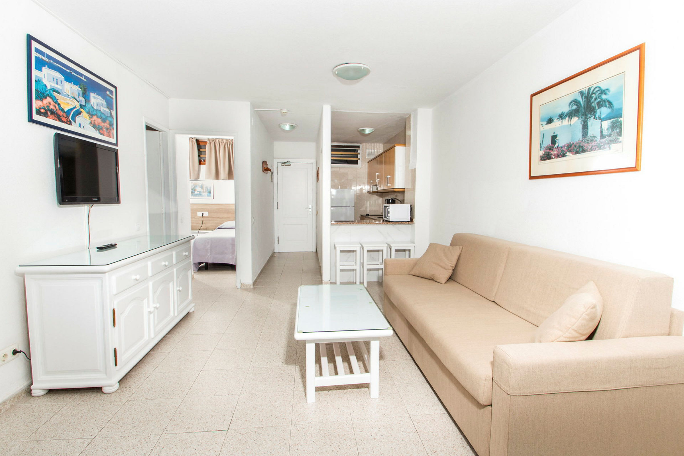 Ett hotellrum med en soffa, soffbord, väggmonterad TV och ett pentry. (AI-genererad text)