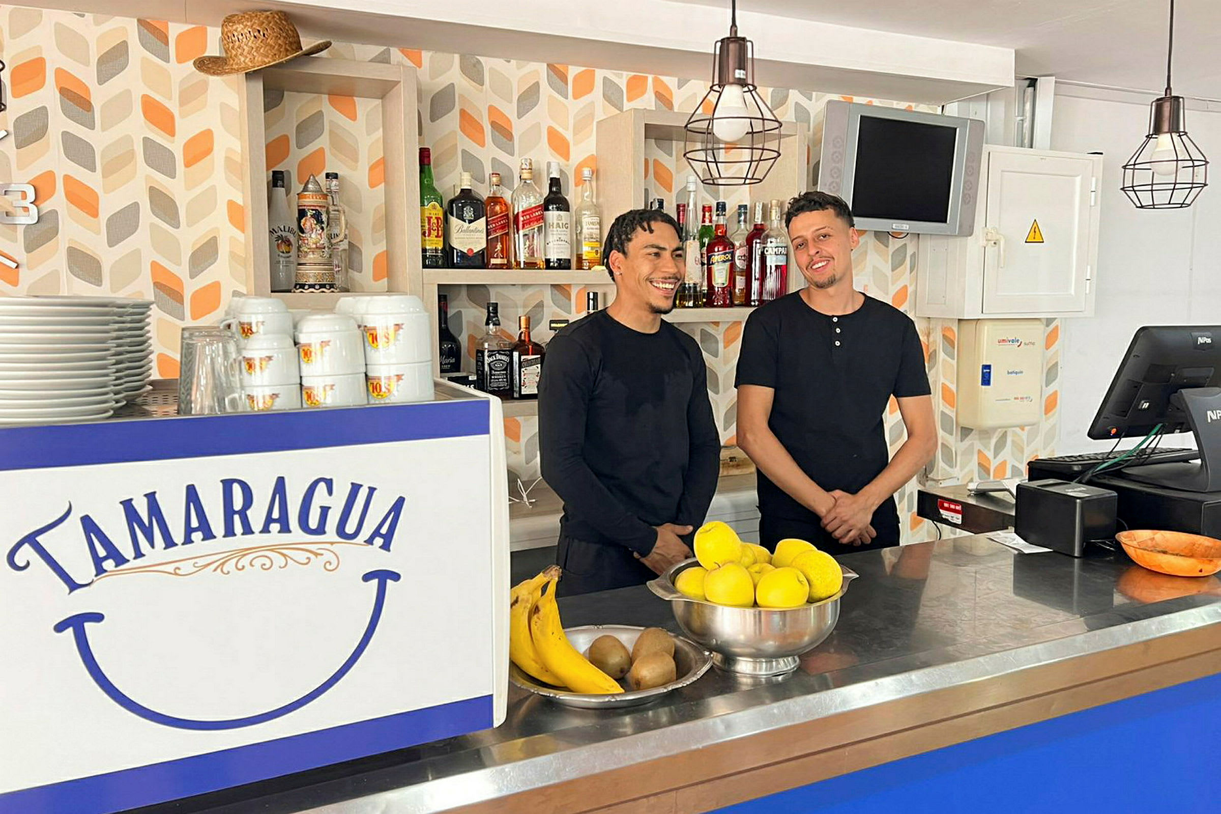 En bar med en disk dekorerad med texten "Tamaragua". På disken finns frukter och porslin. Bakgrunden har hyllor med flaskor. (AI-genererad text)