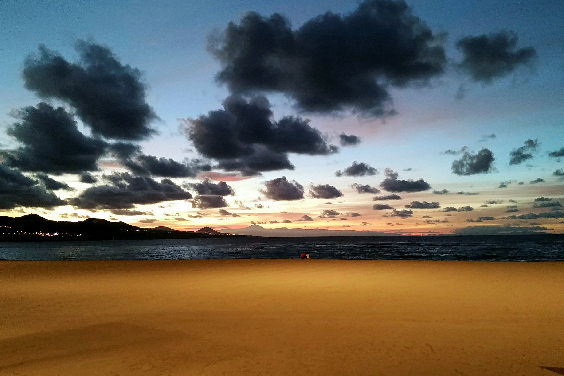 Sandstrand vid havet under en kvällshimmel med moln och solnedgång. (AI-genererad text)
