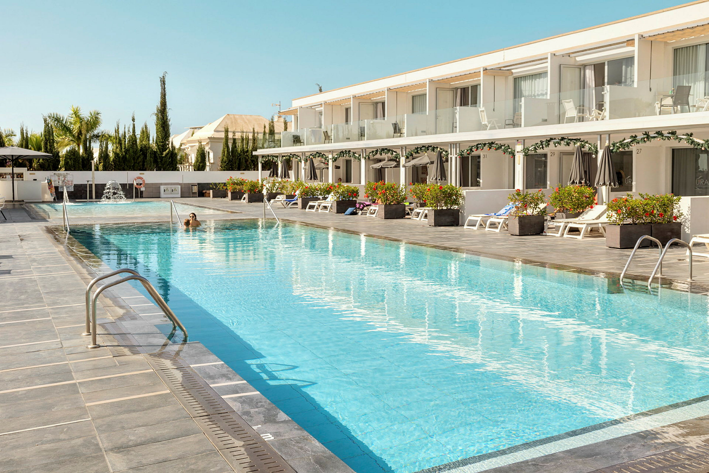 En hotellpool med solstolar och parasoller på sidan. (AI-genererad text)