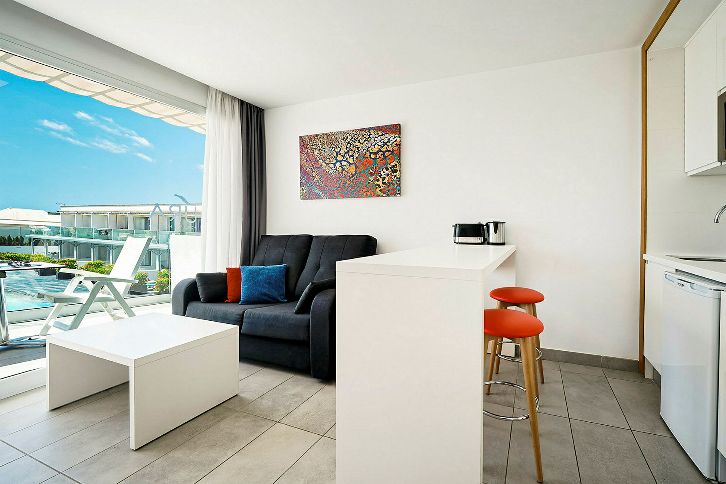 Ett modernt hotellrum med soffa, bord, pentry och en balkong med utsikt. (AI-genererad text)