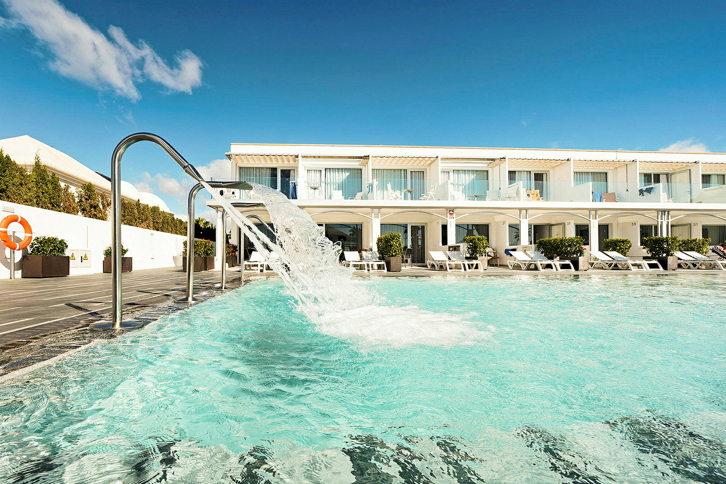 Poolområde med liggstolar och en hotellbyggnad i bakgrunden. (AI-genererad text)