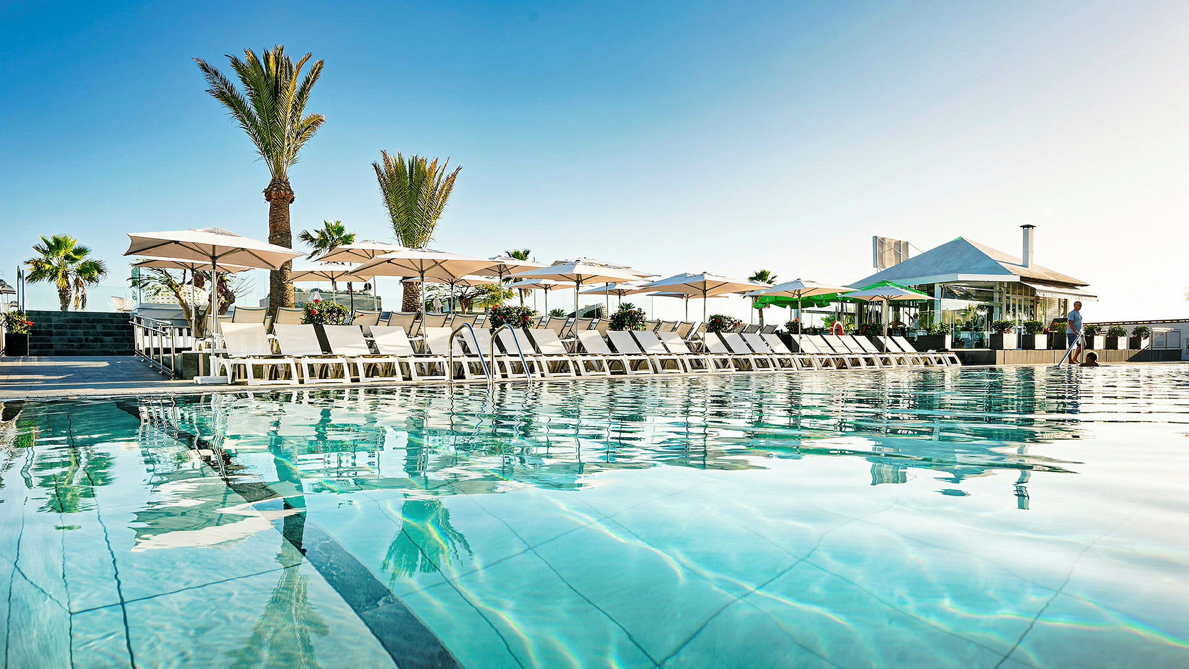 Bild av en pool med solstolar och parasoller vid ett hotell. (AI-genererad text)