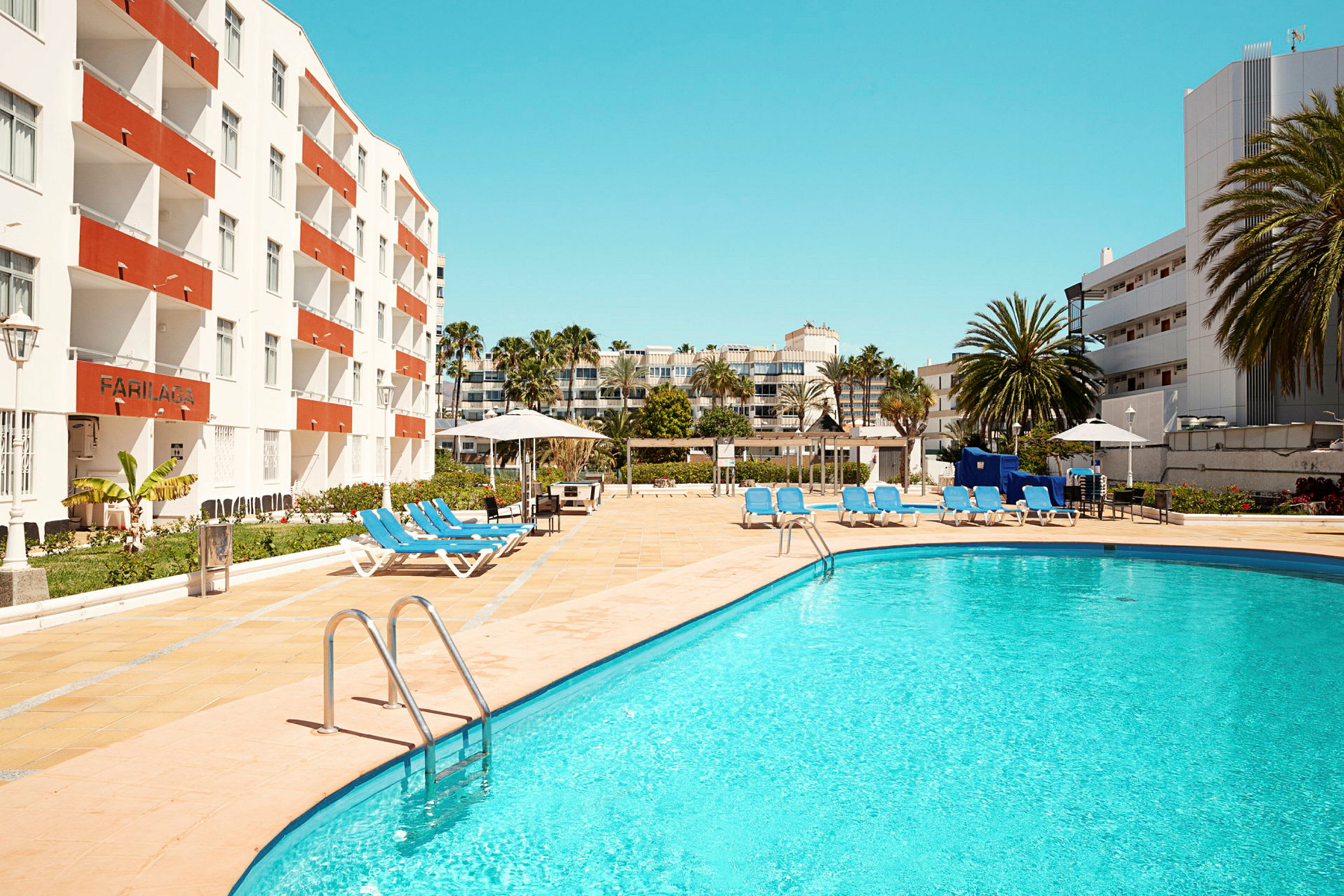 Utomhuspool med solstolar och omkringliggande hotellbyggnader. (AI-genererad text)