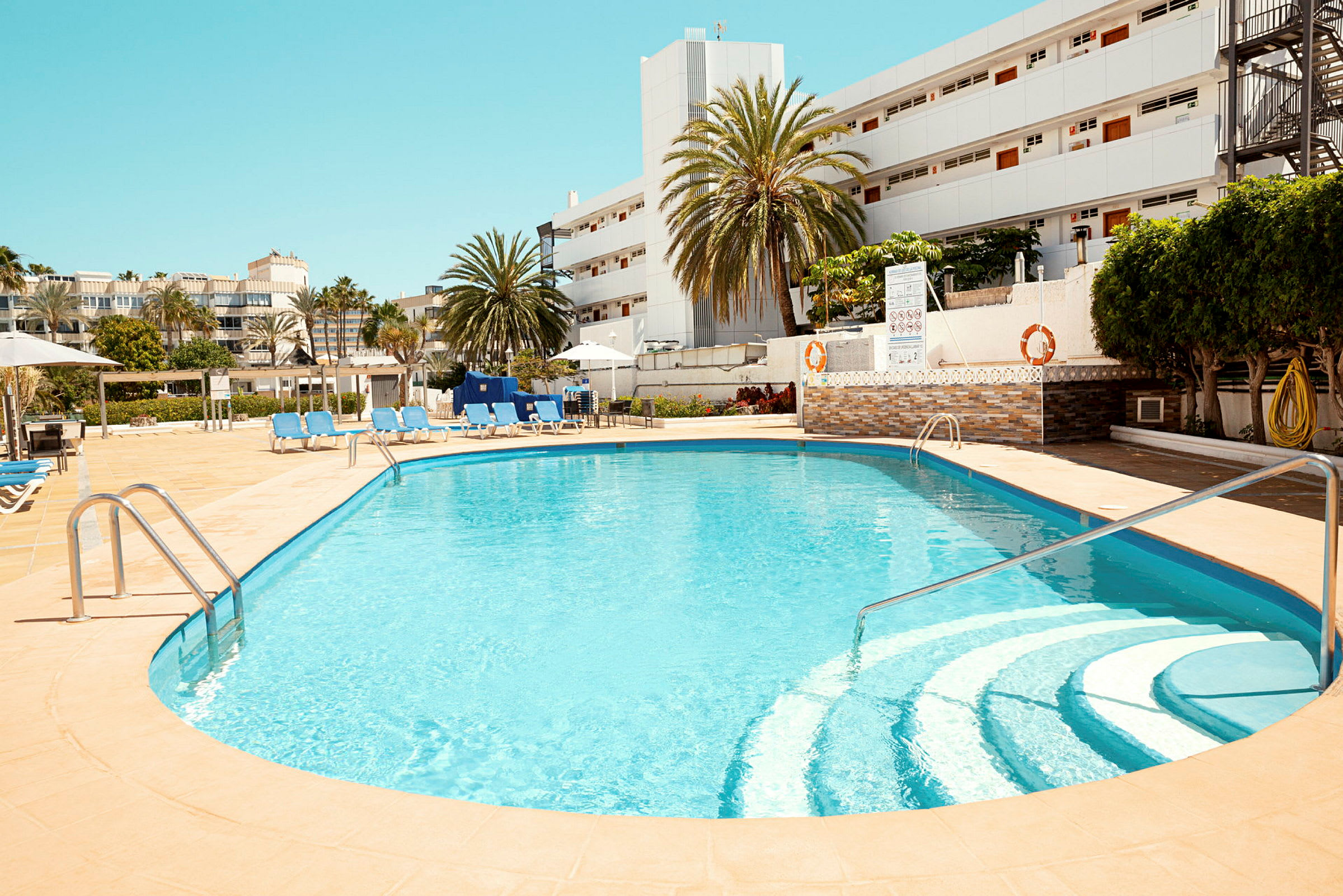 Utomhuspool med stolar och solstolar runt, i hotellmiljö. (AI-genererad text)