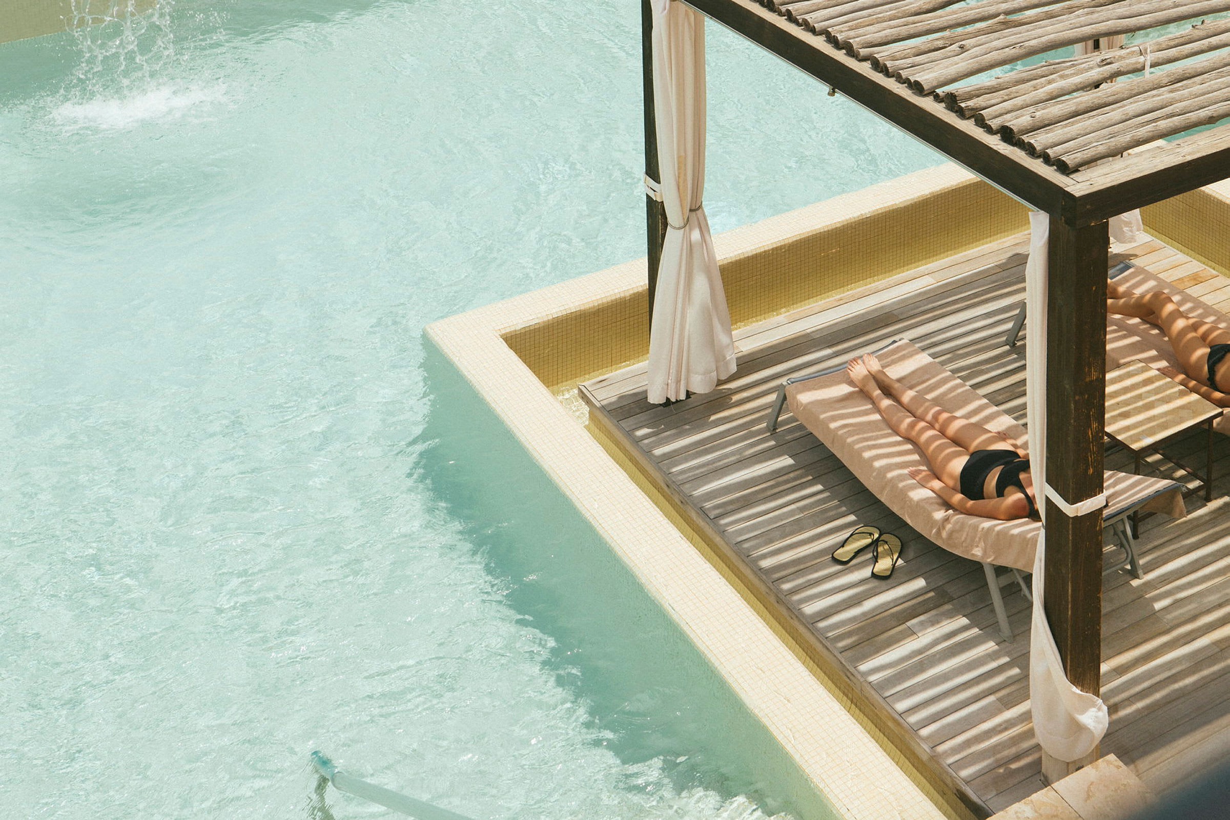 En person ligger på en solbädd i skuggan vid en swimmingpool. (AI-genererad text)