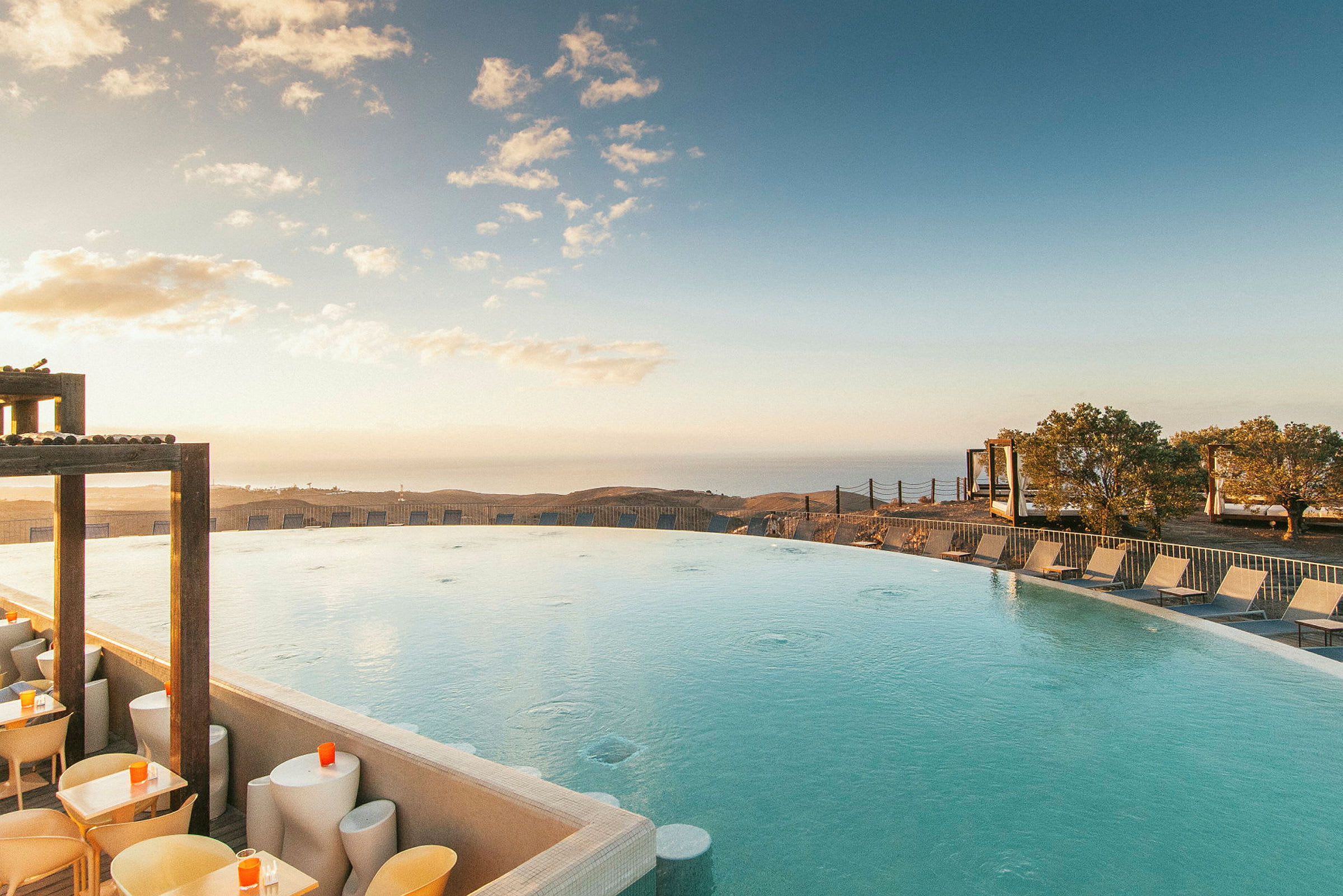 Blå swimmingpool med solstolar och utsikt över havet och träd. (AI-genererad text)
