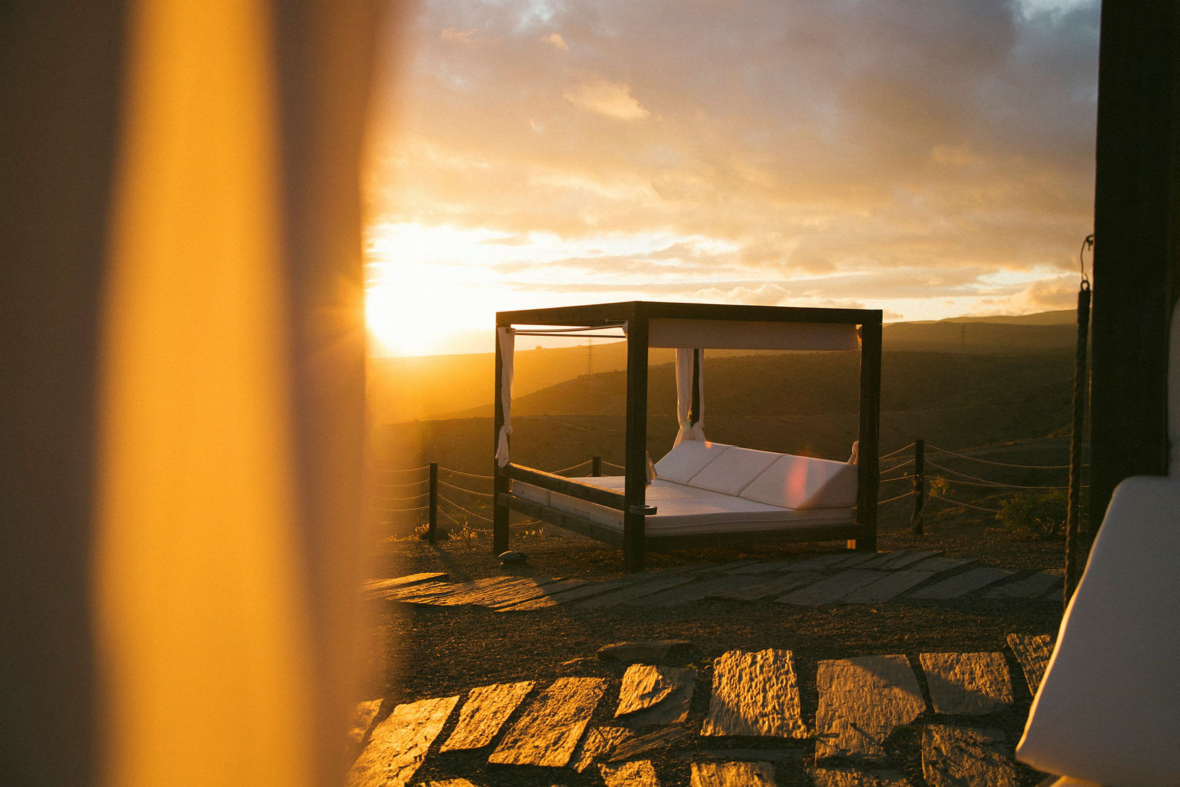 En himmelssäng på en terrass med solnedgång i bakgrunden. (AI-genererad text)