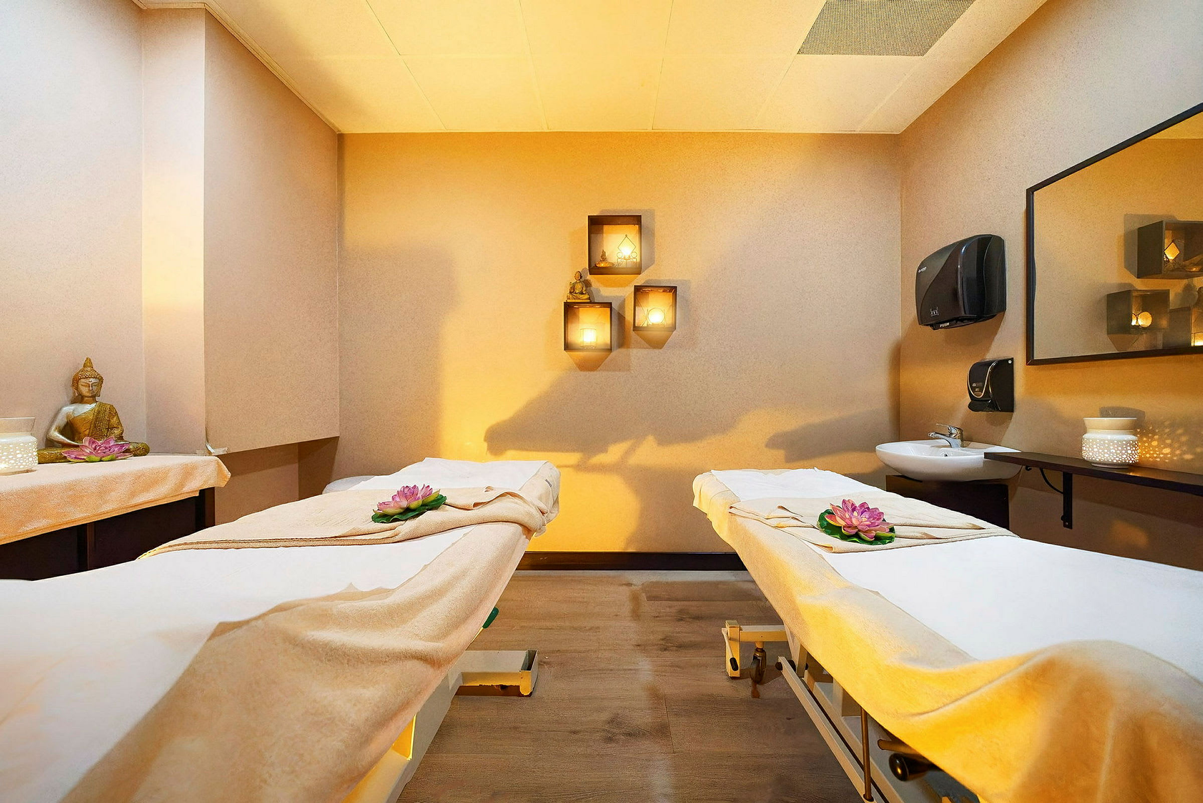 Rum med två massagesängar dekorerade med blommor, en Buddha-staty på hyllan och mjuk belysning. (AI-genererad text)