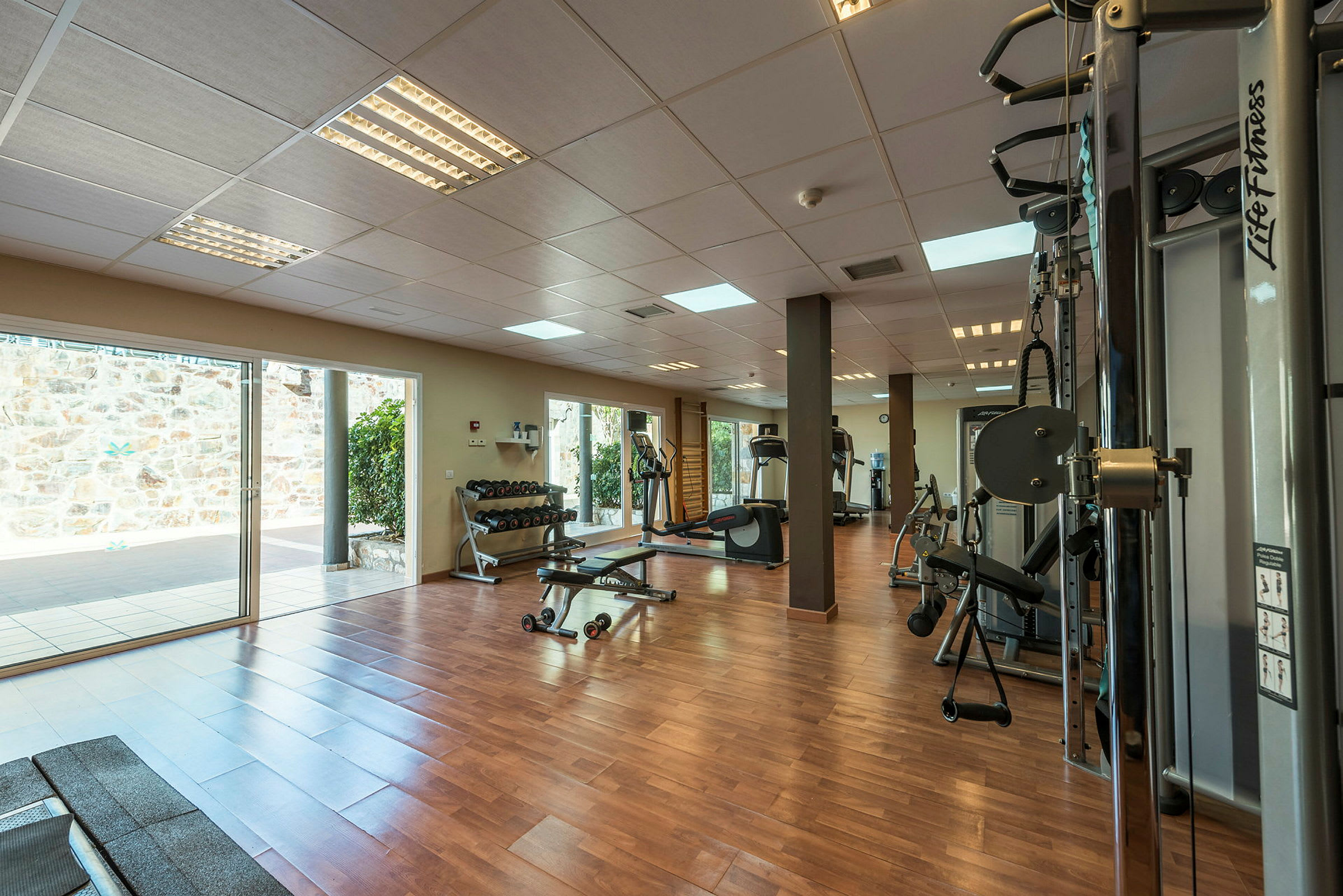 Gym med träningsutrustning och stora fönster mot en utomhusterrass. (AI-genererad text)