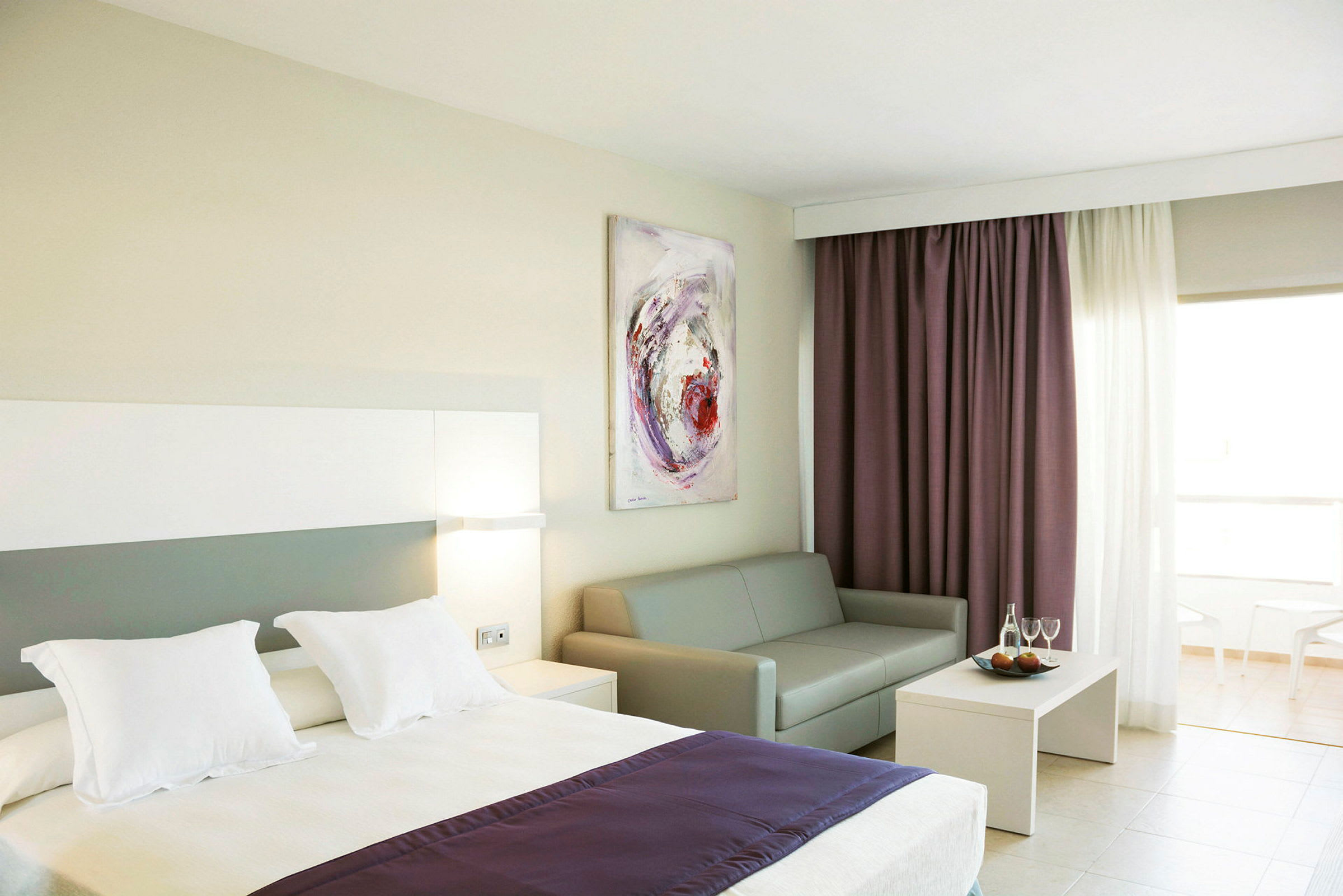 Hotellrum med säng, soffa, soffbord och gardiner. (AI-genererad text)