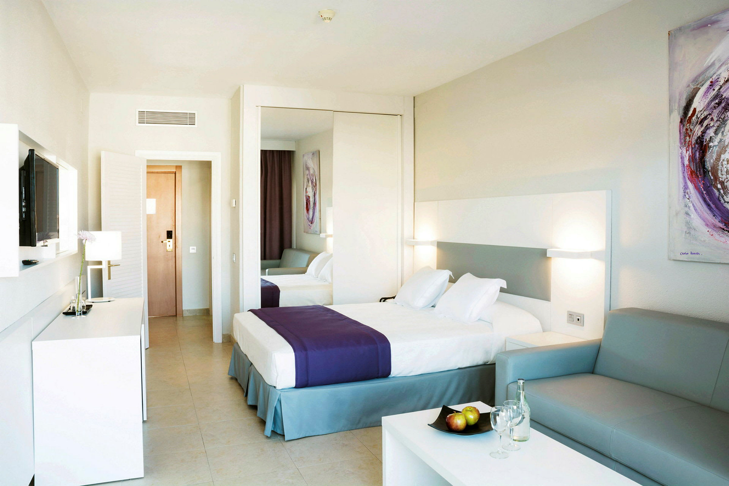 Hotellrum med dubbelsäng, lila pläd, soffa och dekorationer. (AI-genererad text)