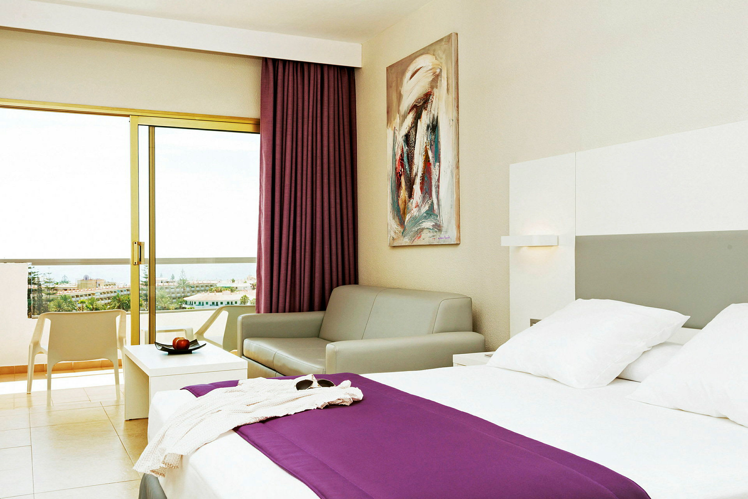Hotellrum med en säng, en soffa och en balkong med utsikt. (AI-genererad text)