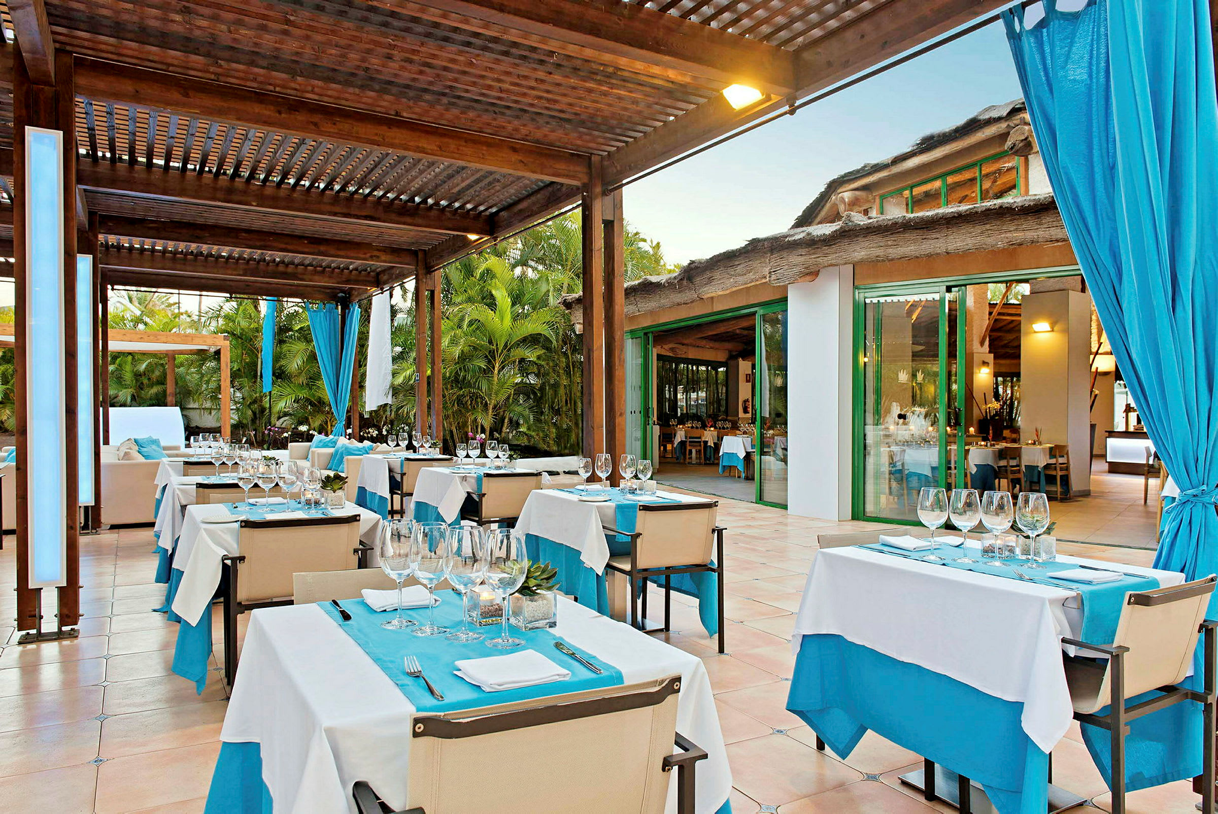 En utomhusrestaurang med dukade bord under en träpergola. (AI-genererad text)