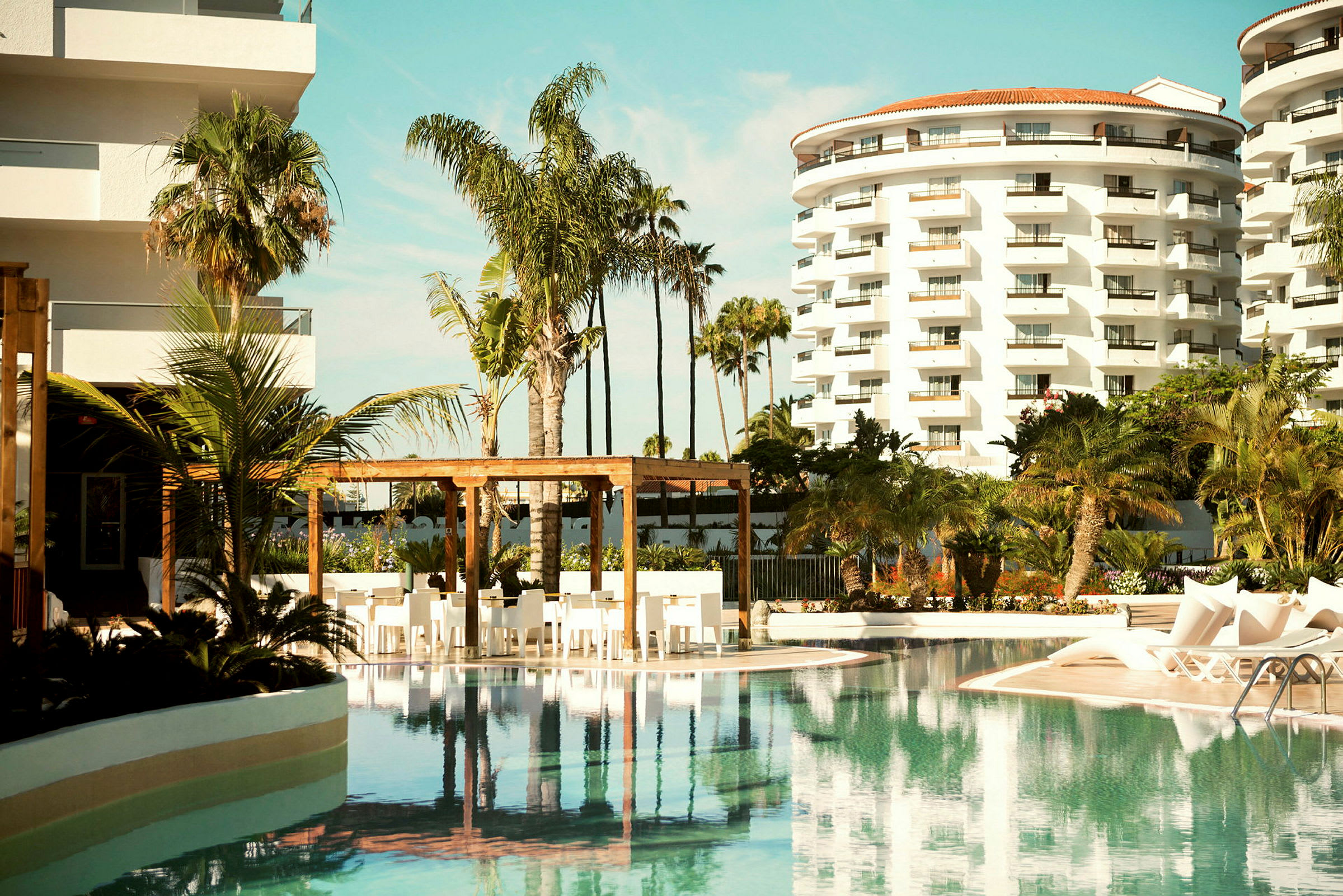 Solbelyst hotellpool med palmer och byggnader i bakgrunden. (AI-genererad text)