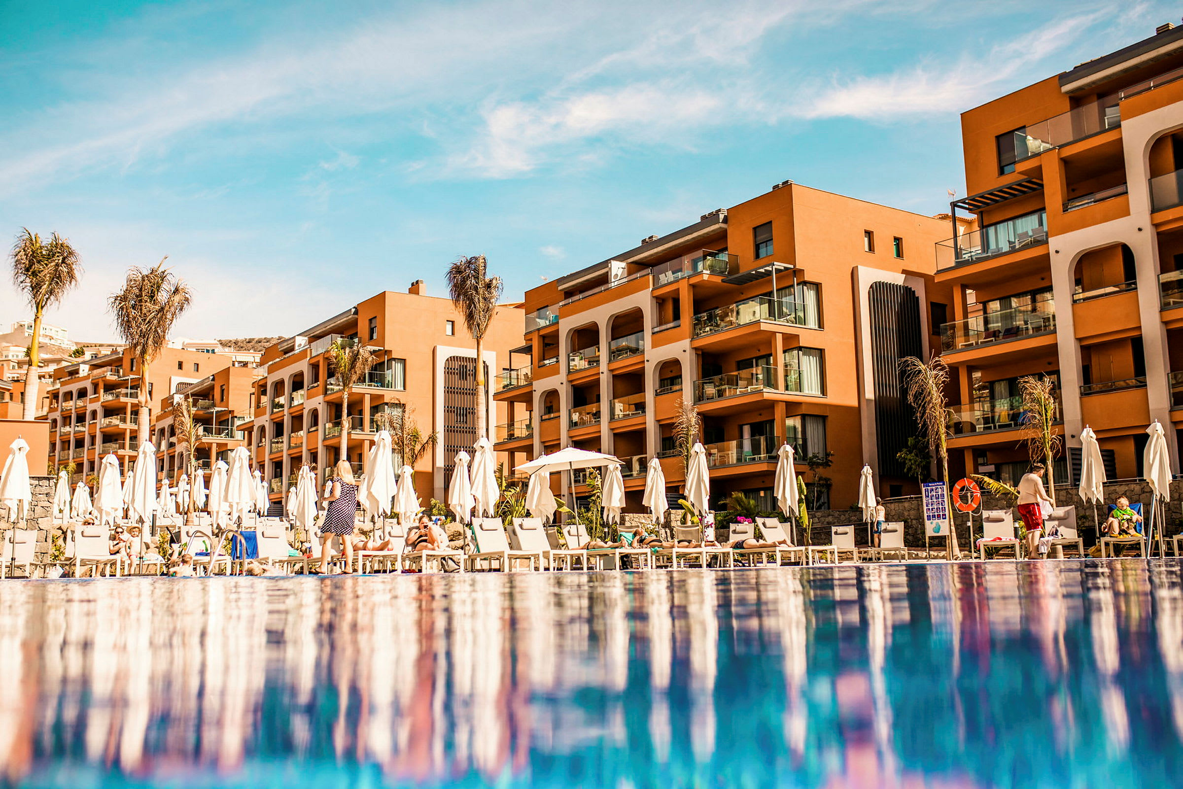 Hotellbyggnad med solstolar och parasoller vid poolen. (AI-genererad text)