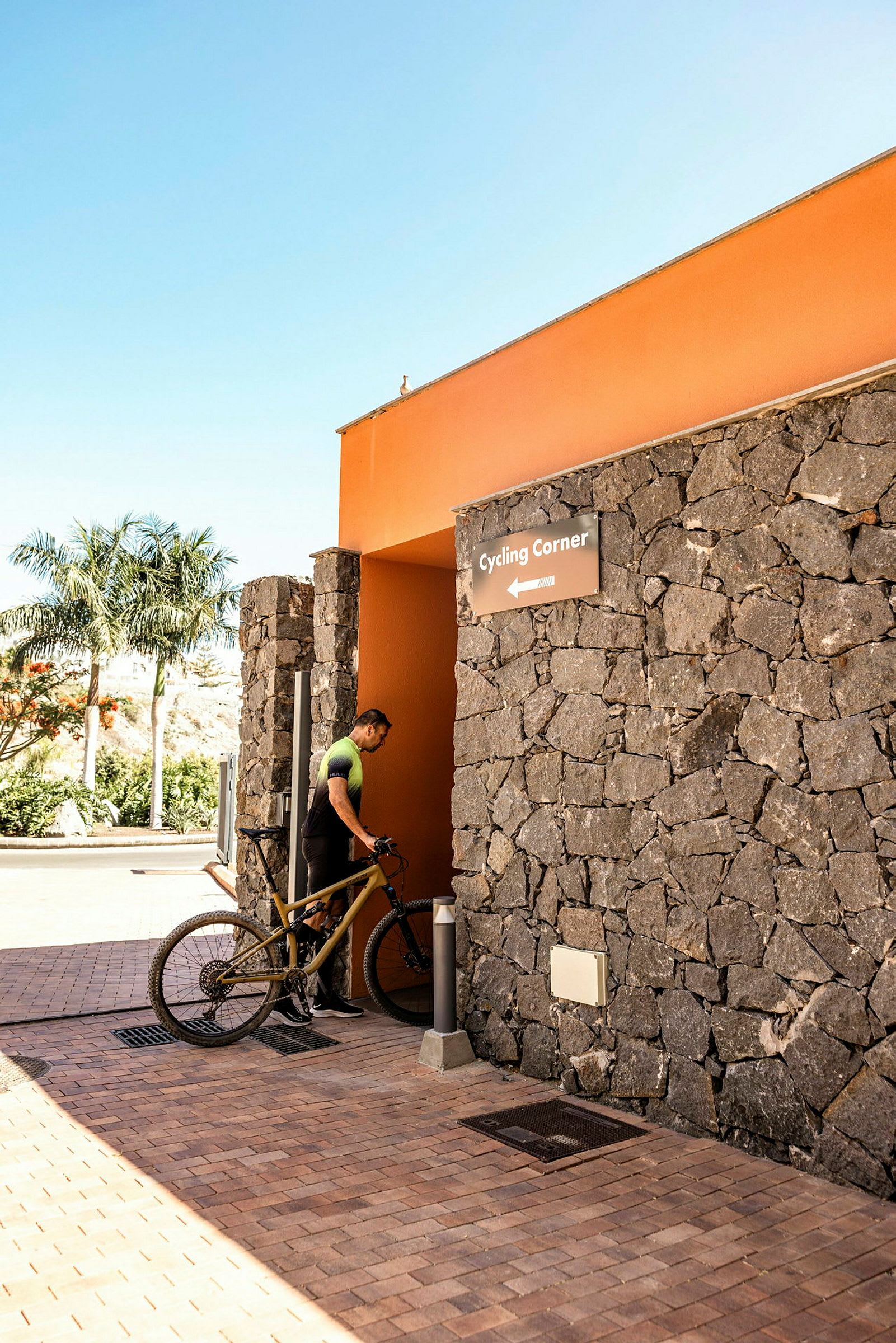 En person med cykel vid ingången till ett stenbyggt område märkt 'Cycling Corner'. (AI-genererad text)