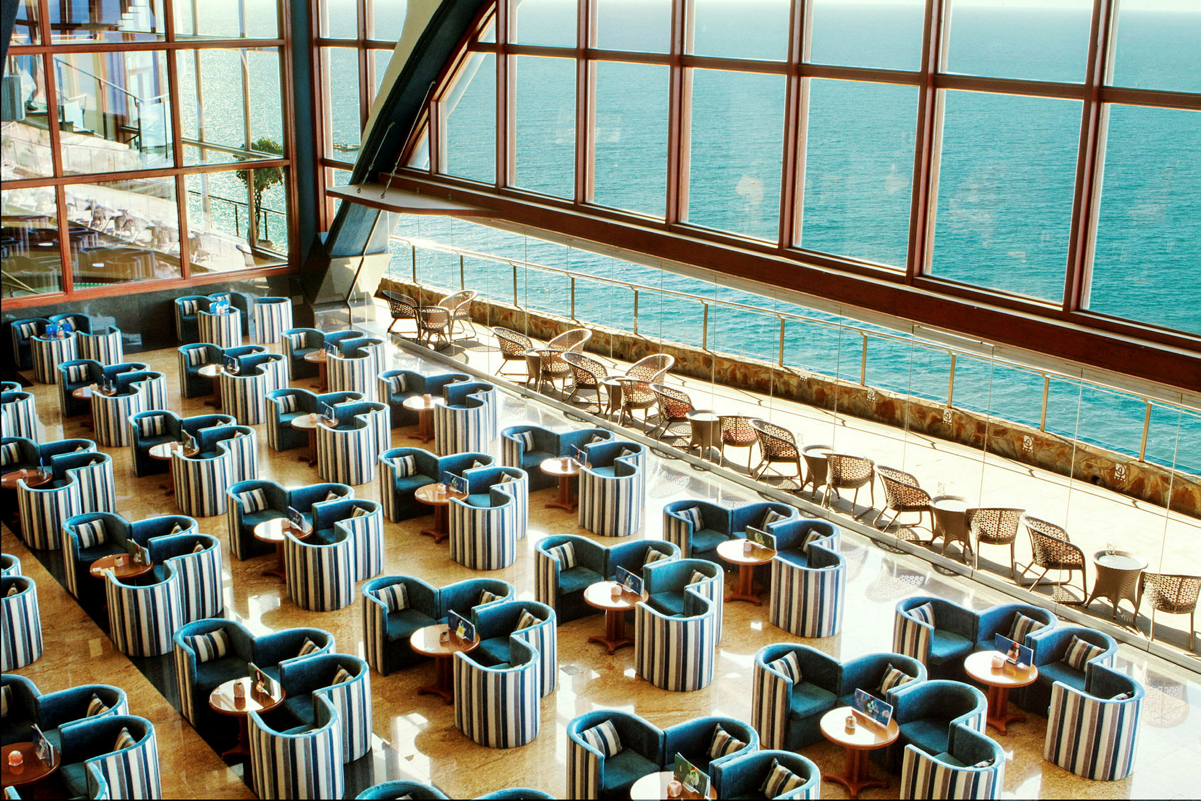 En inomhuslounge med ordnade sittplatser och en stor fönstervy mot havet. (AI-genererad text)