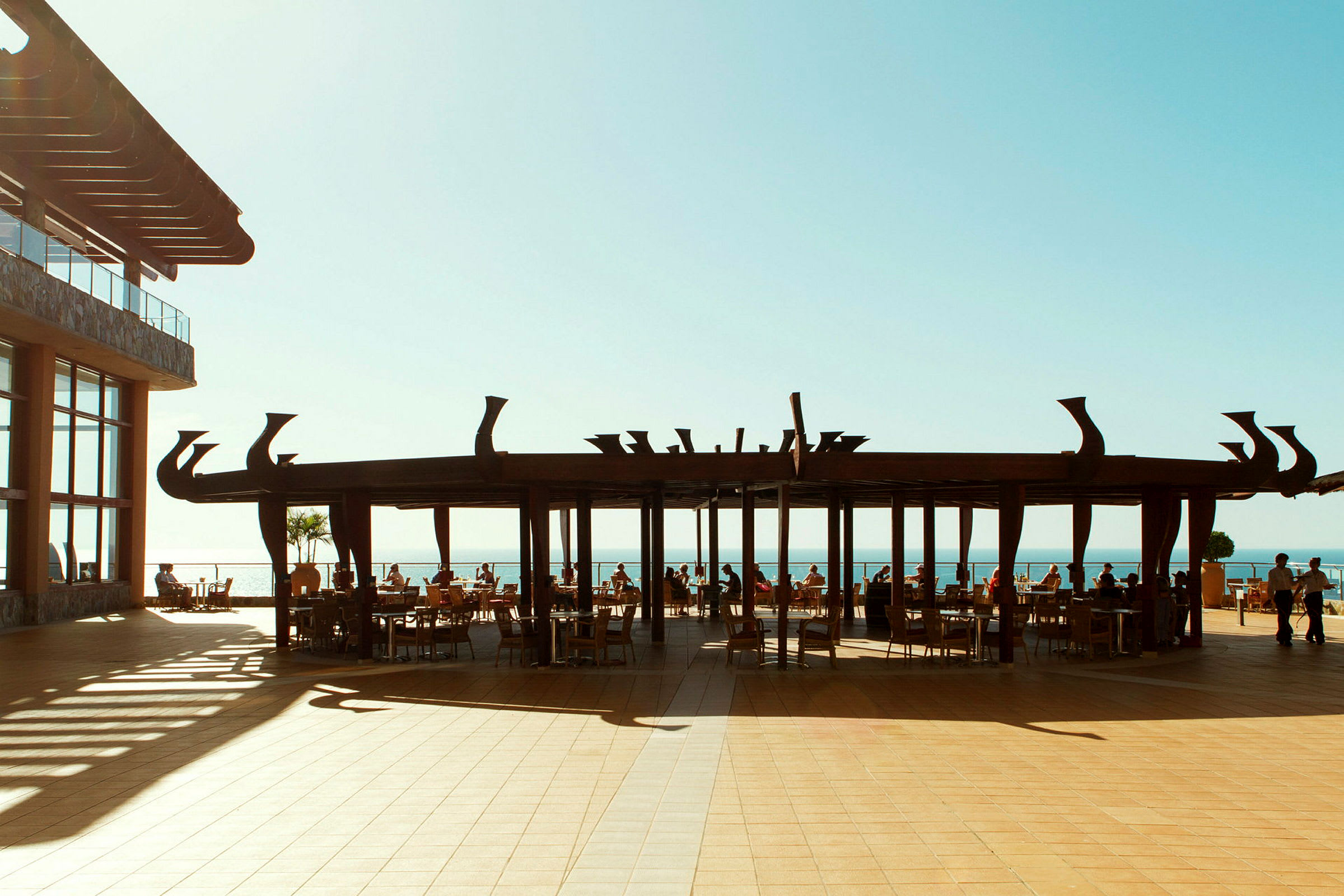 En utomhusrestaurang med utsikt över havet under en stiliserad pergola. (AI-genererad text)