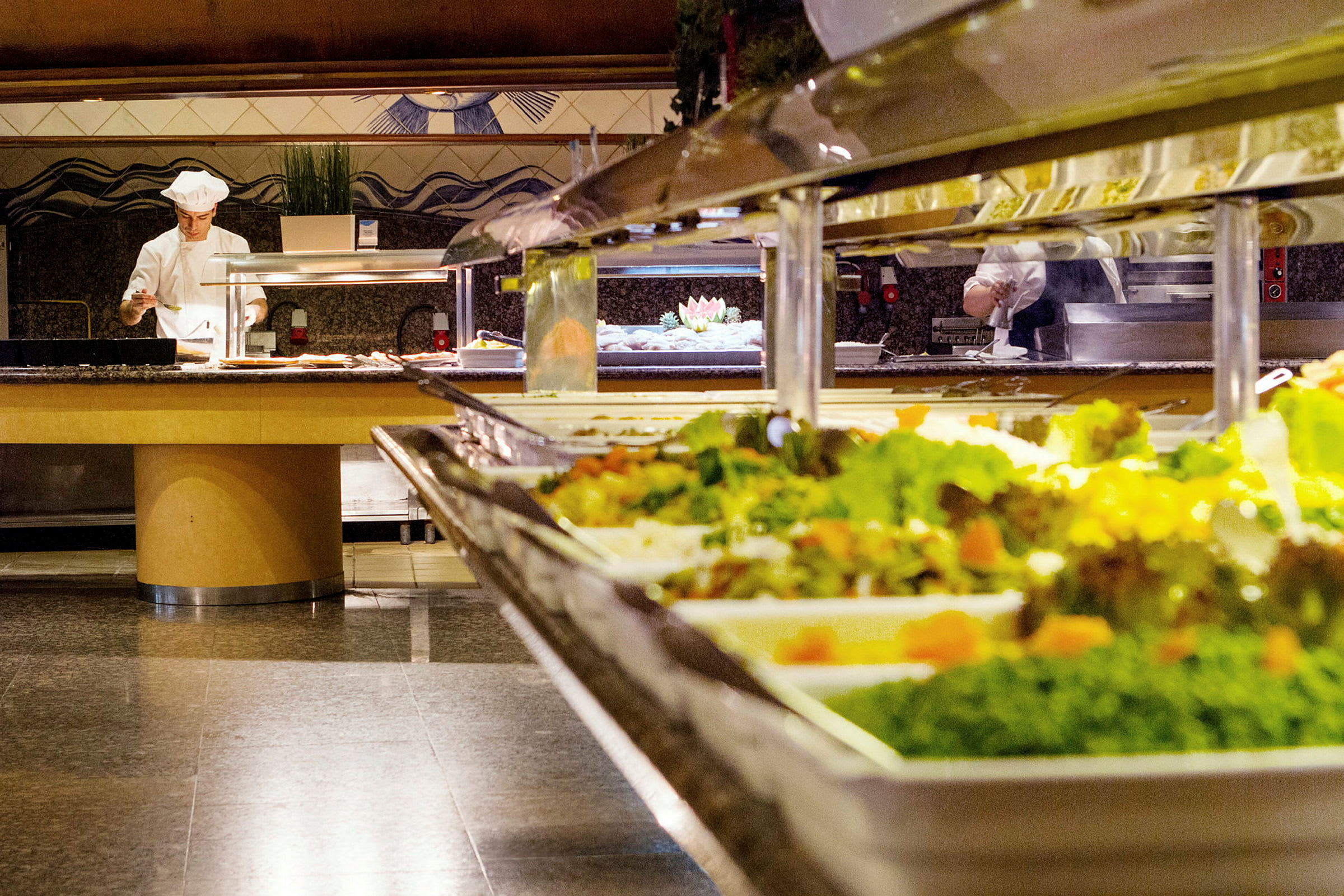 Buffébord med sallader och en kock som tillagar mat i bakgrunden. (AI-genererad text)