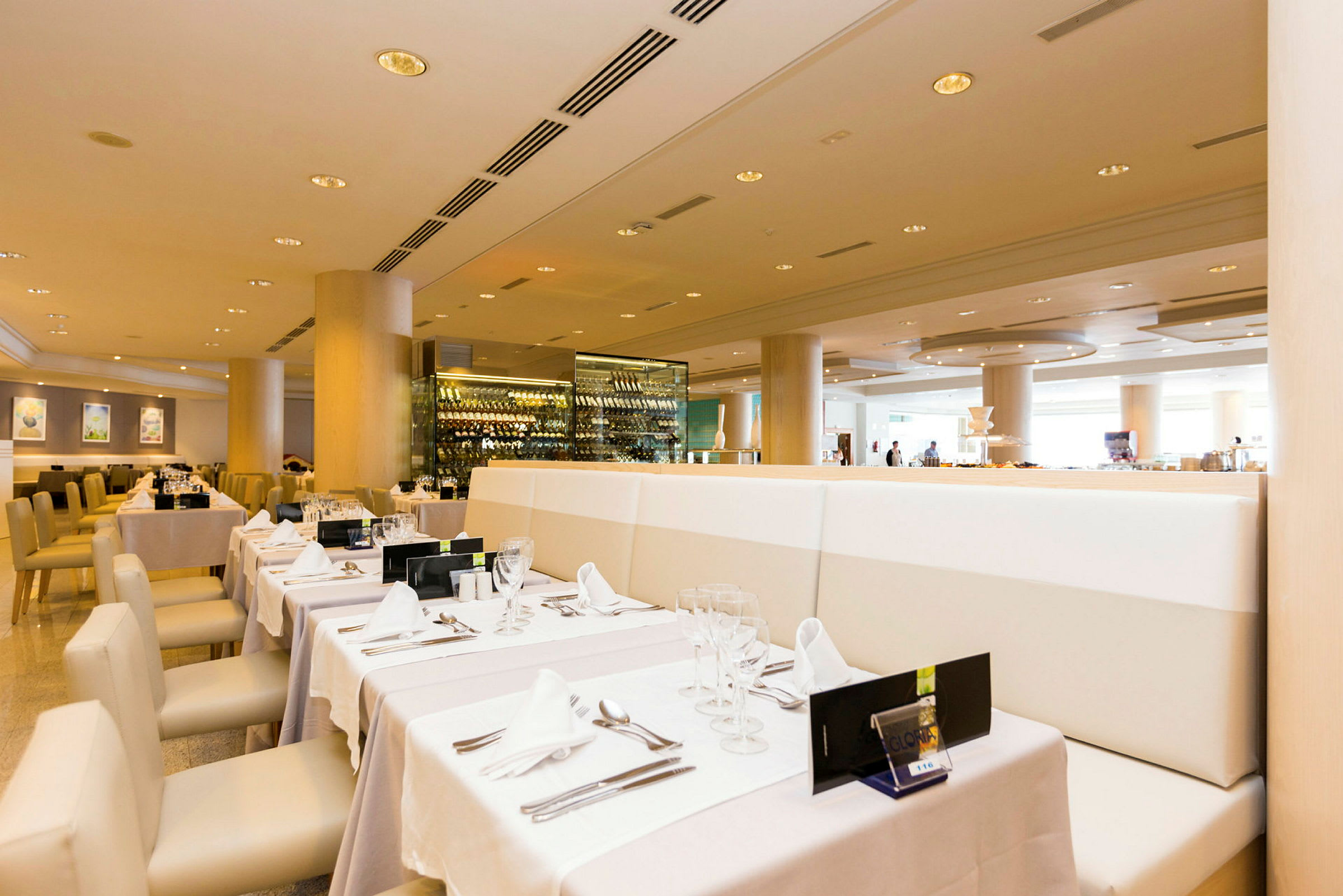 En restaurang med eleganta bord dukade med vita dukar och glas. En vinförvaring syns i bakgrunden. (AI-genererad text)