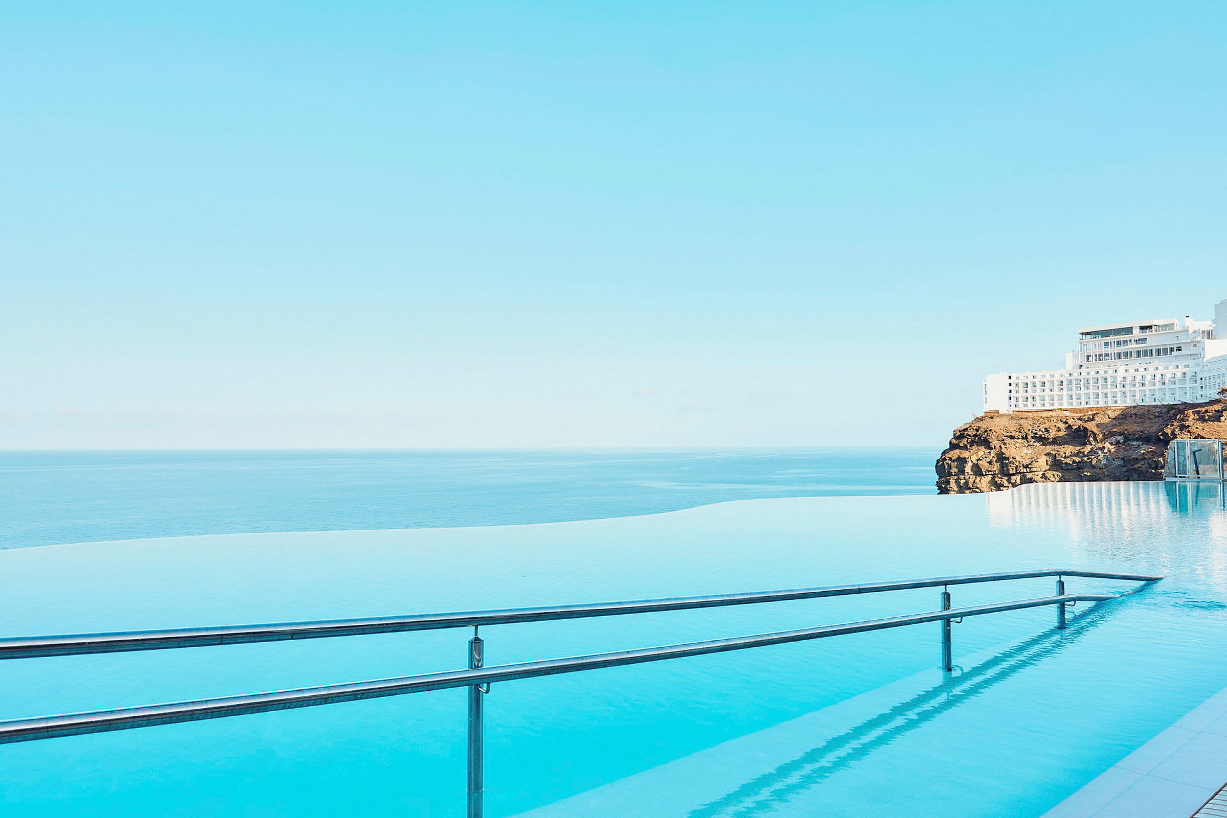 Infinitypool med utsikt över havet och en byggnad på en klippa. (AI-genererad text)