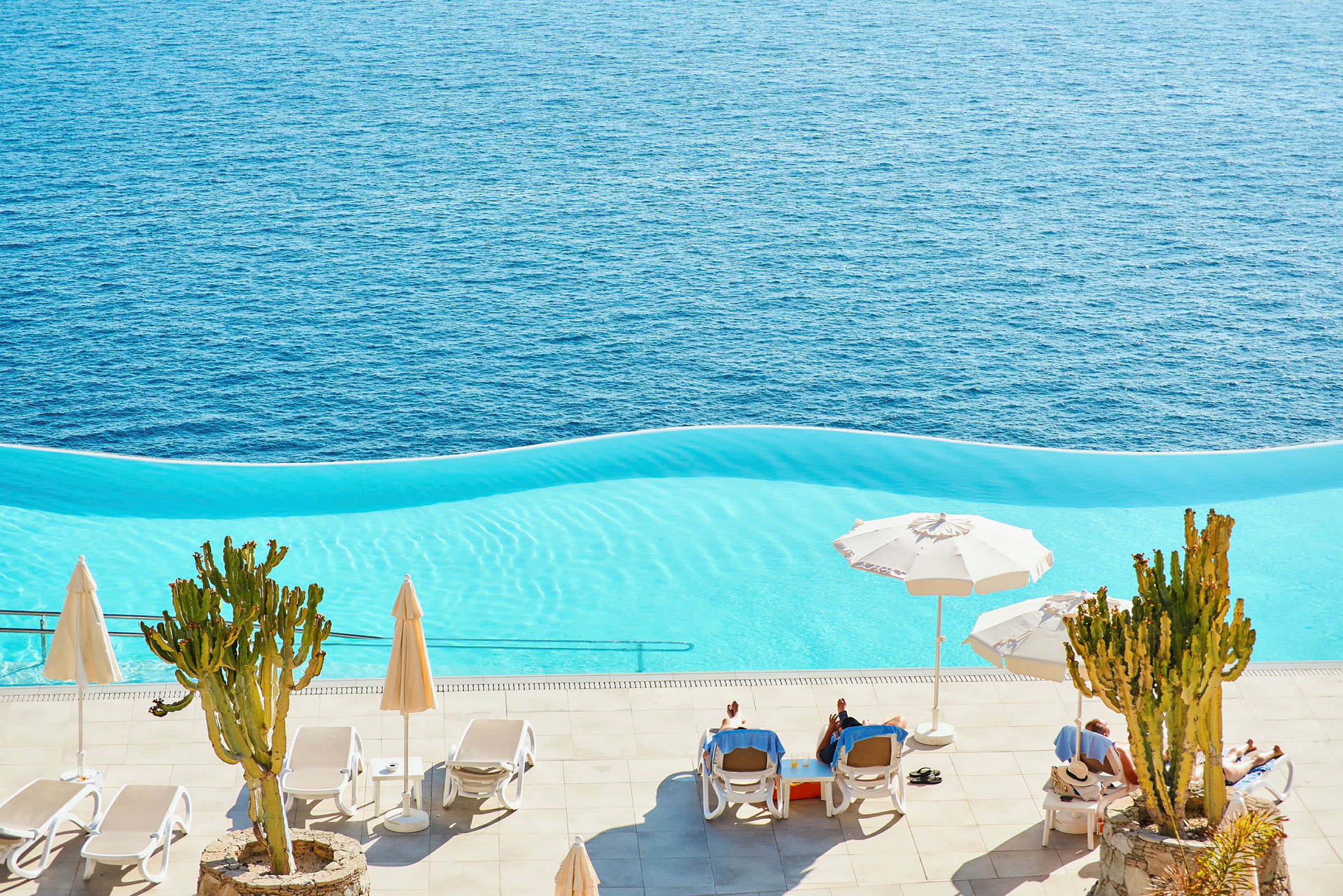 Infinitypool med utsikt över havet, parasoller och solstolar. (AI-genererad text)