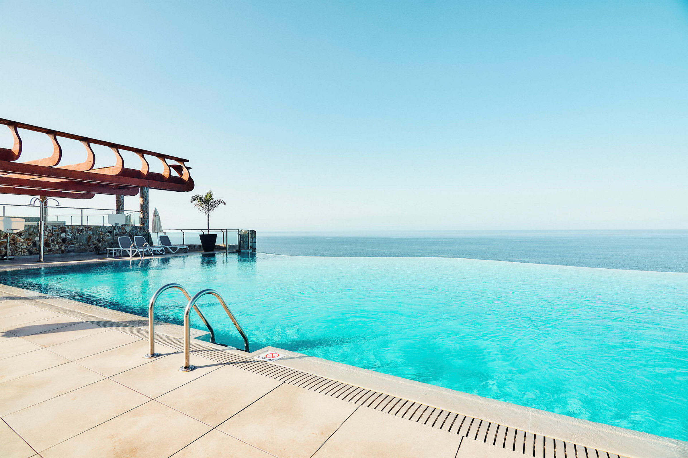 En infinitypool med havsutsikt och solstolar vid kanten. (AI-genererad text)
