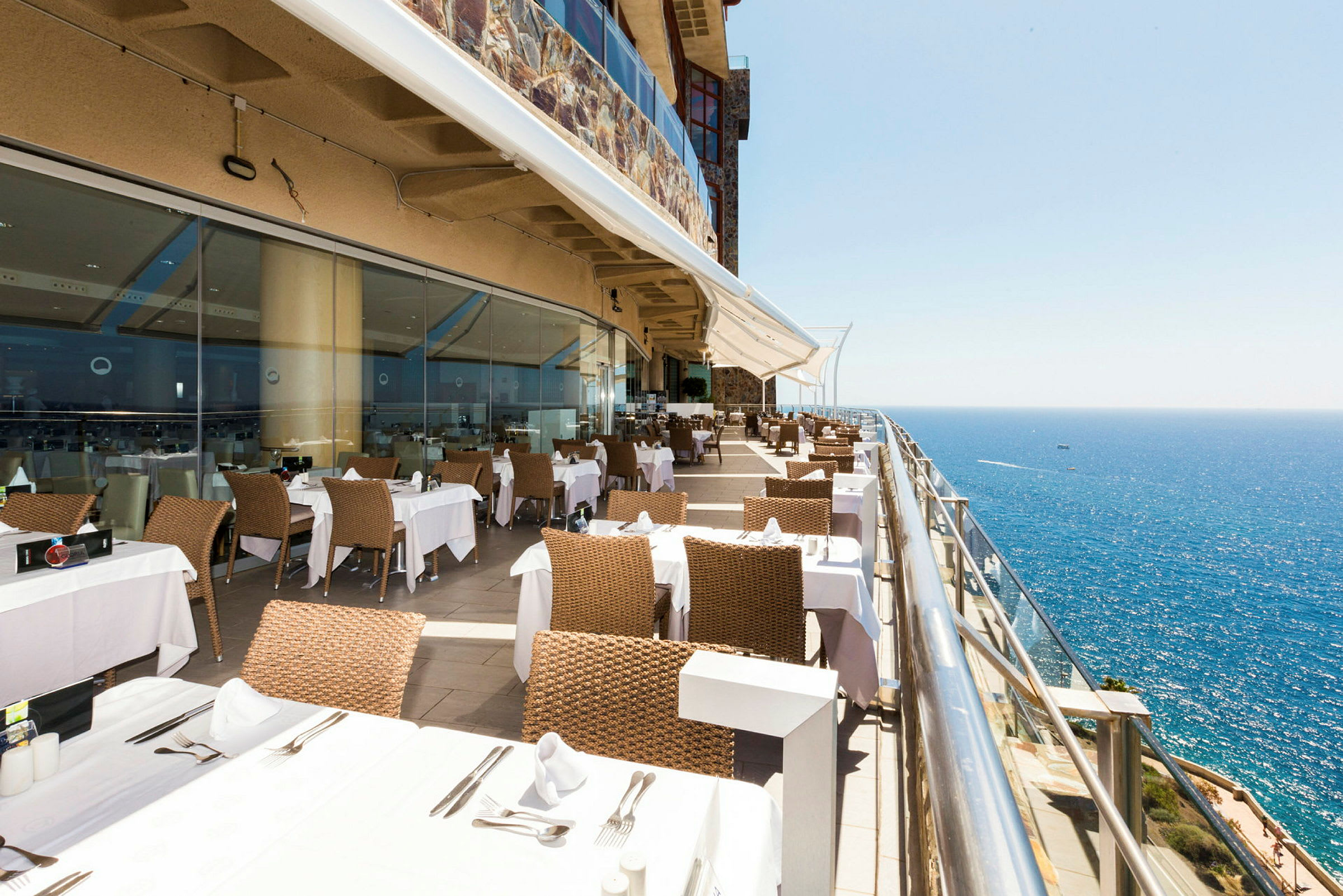 Restaurang med bord och stolar på en terrass med utsikt över havet. (AI-genererad text)
