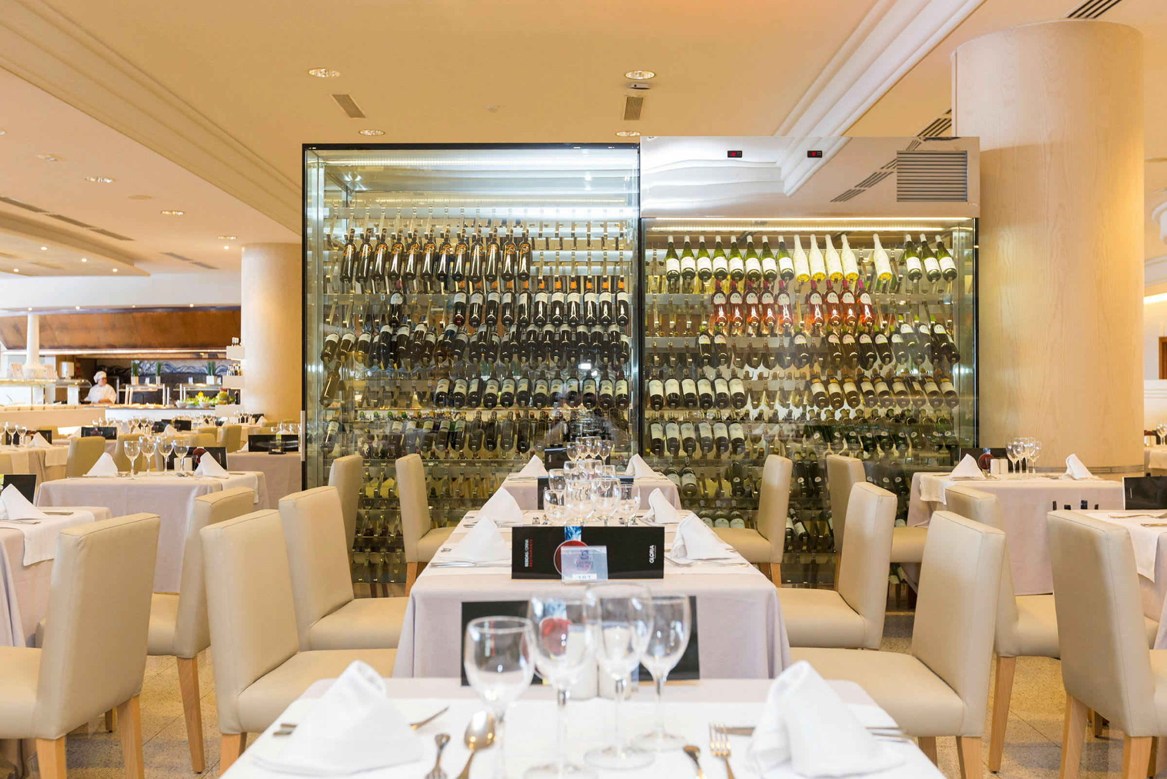 En restaurang med dukade bord framför ett glasvägg med en samling vinflaskor. (AI-genererad text)