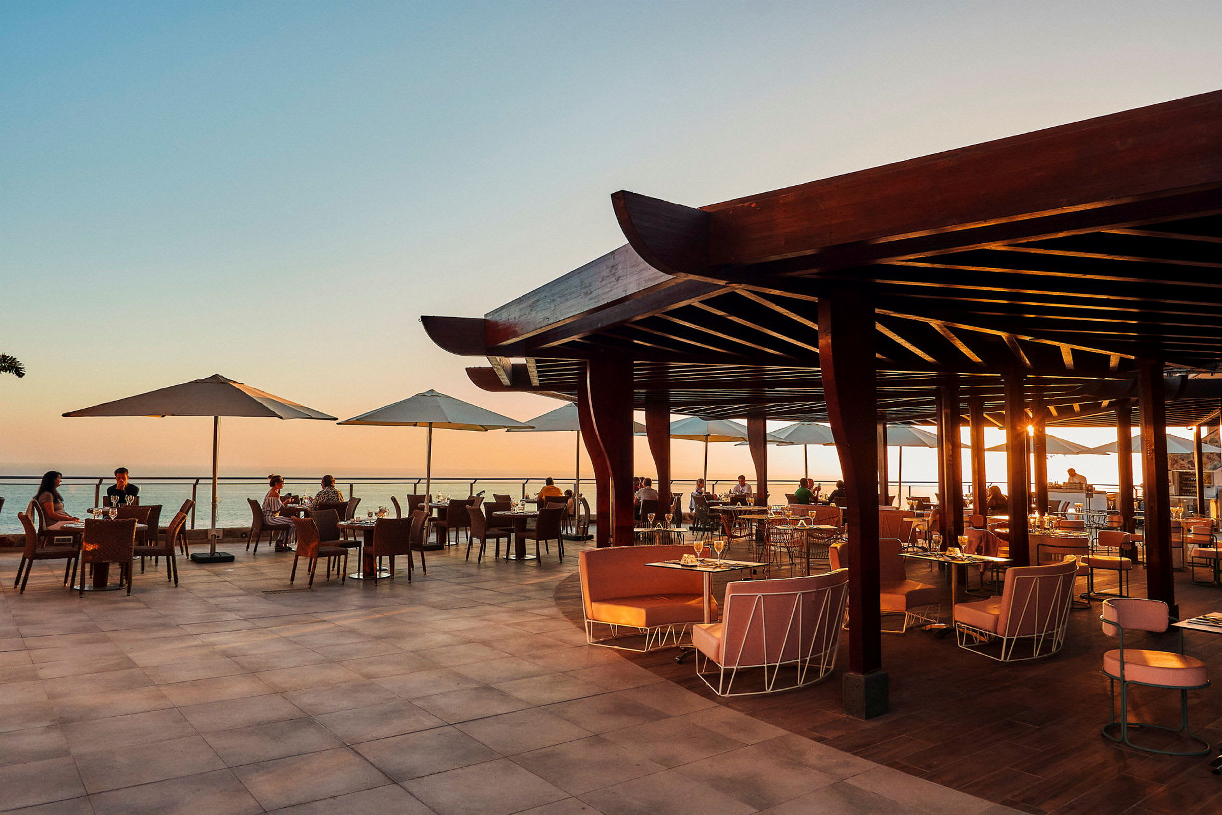 Öppen restaurangterrass med utsikt över havet vid solnedgång. (AI-genererad text)