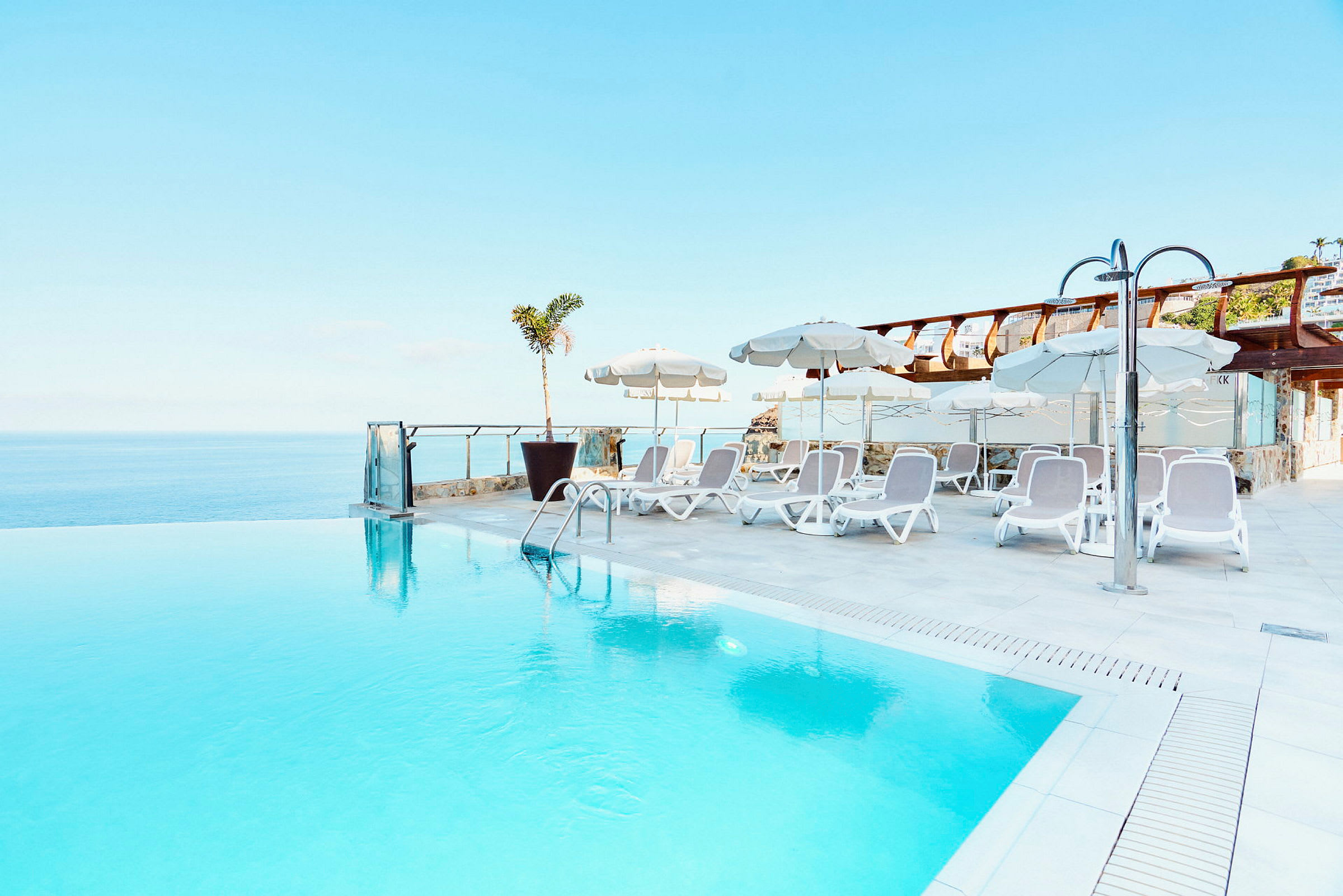 En infinitypool med solstolar och parasoll vid kanten, utsikt över havet. (AI-genererad text)