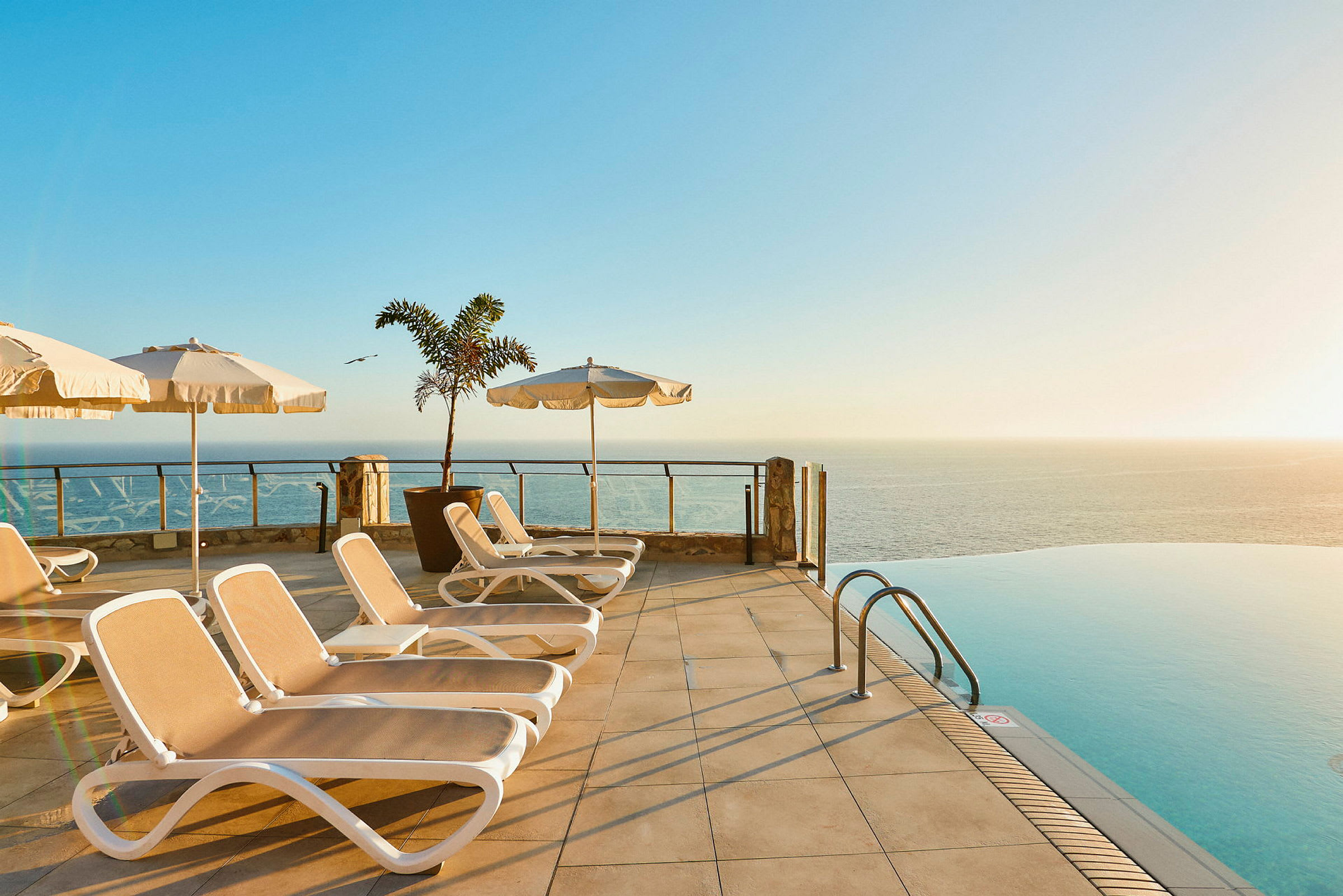 Solstolar och parasoller vid en infinitypool med utsikt över havet. (AI-genererad text)