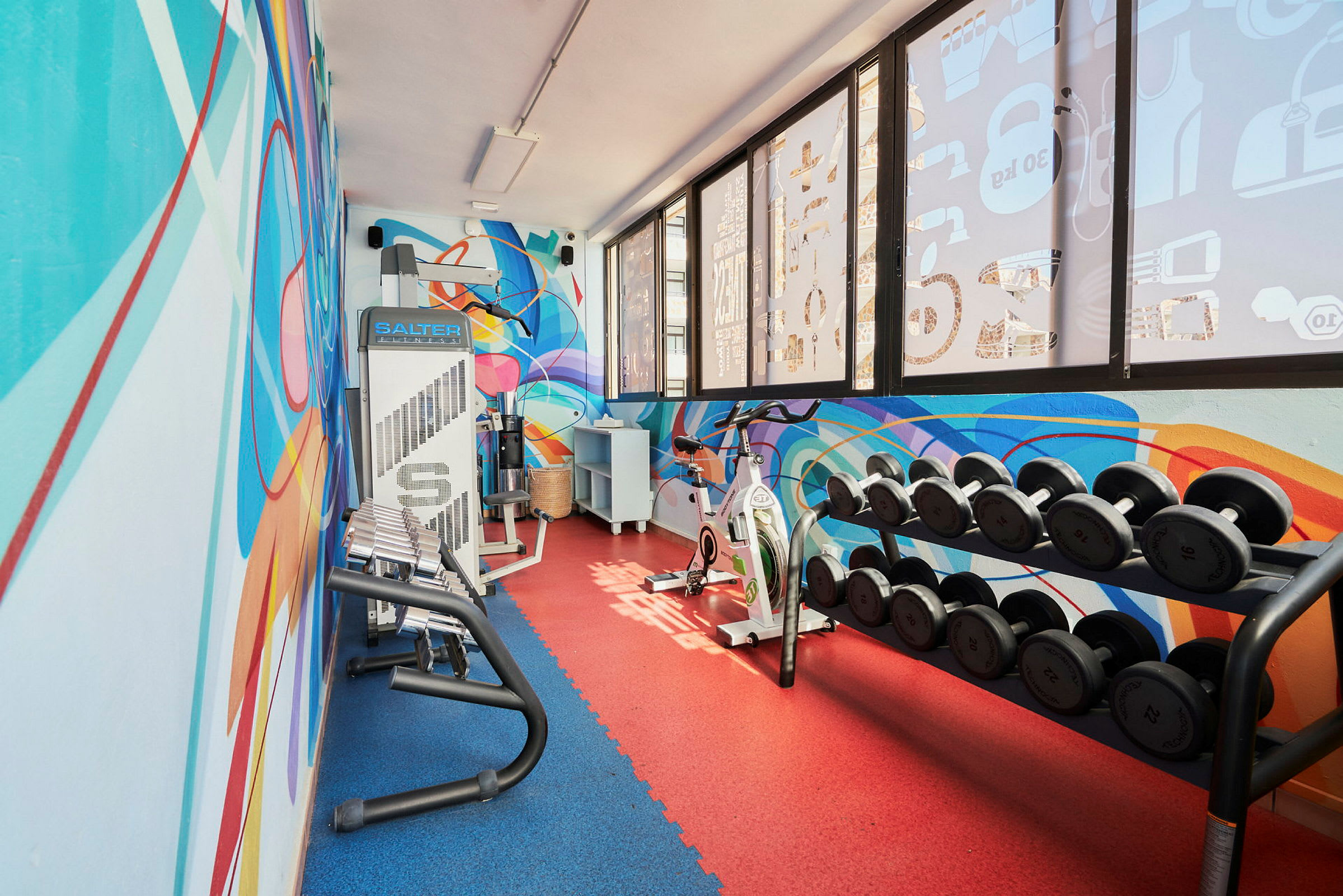 Ett modernt gym med färgglada väggmålningar, vikter och träningsmaskiner. (AI-genererad text)