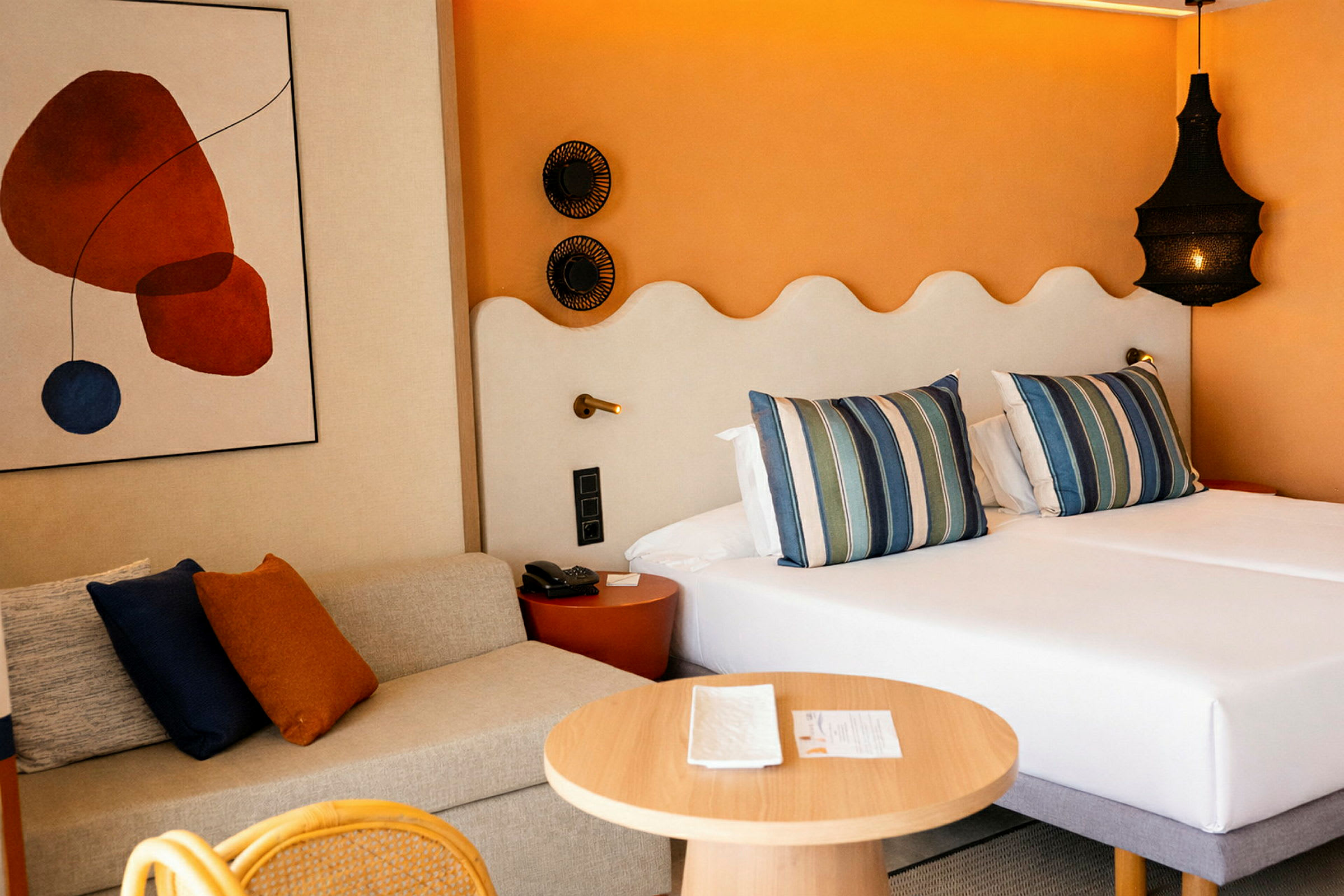 Ett hotellrum med två bäddar, bredvid en soffa och ett runt träbord. (AI-genererad text)