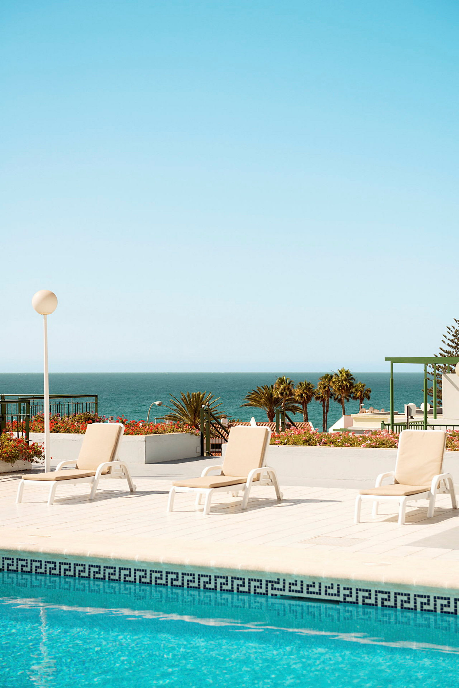 Bild på en pool med solstolar och havet i bakgrunden. (AI-genererad text)